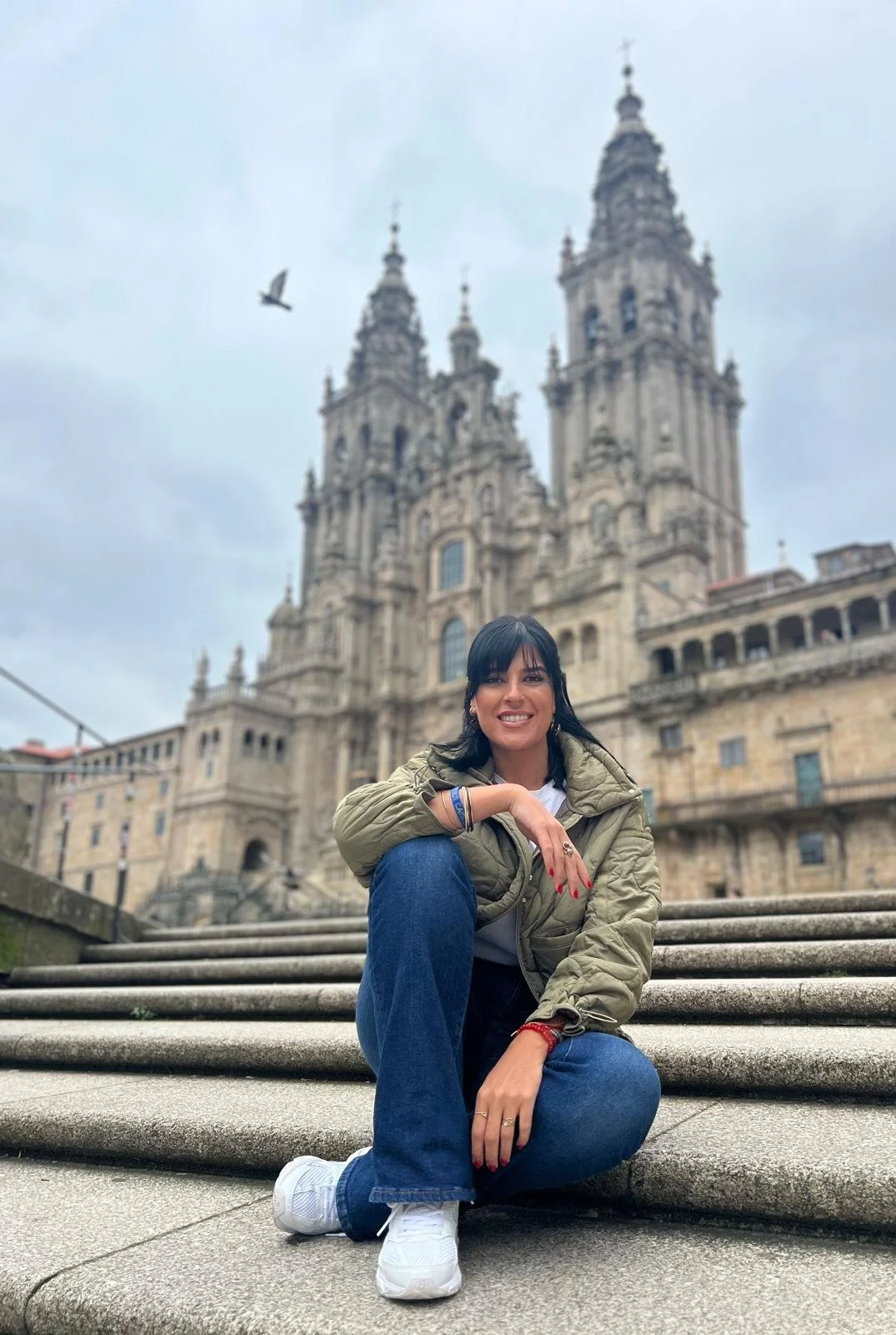 Mujer sonriendo sentada en las escaleras frente a una catedral antigua en una ciudad de México.