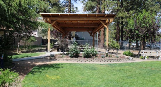 Vivian Null Park, a wooden gazebo stands in a lush garden with green grass and surrounding trees. A picnic table is underneath, creating a peaceful, inviting atmosphere.