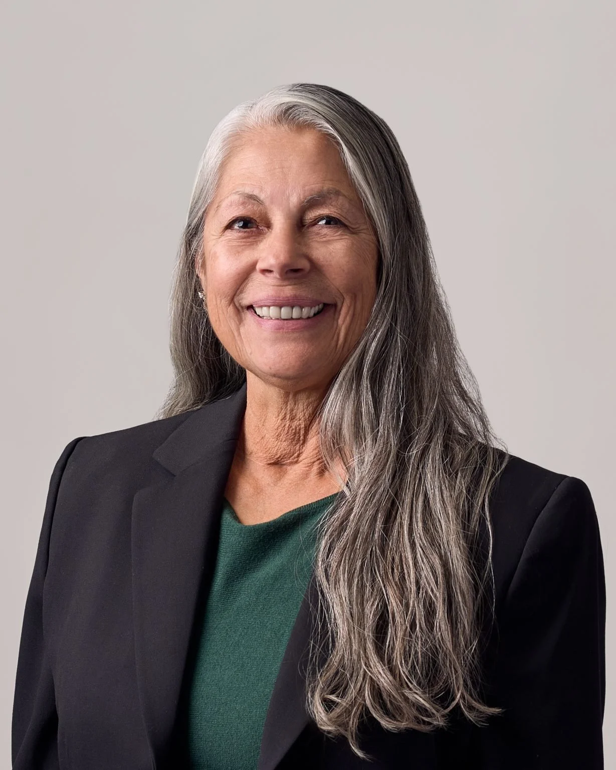 Martha McFauls, a smiling older woman with long gray hair wearing a black blazer and green top. She stands against a plain background, conveying warmth and confidence.