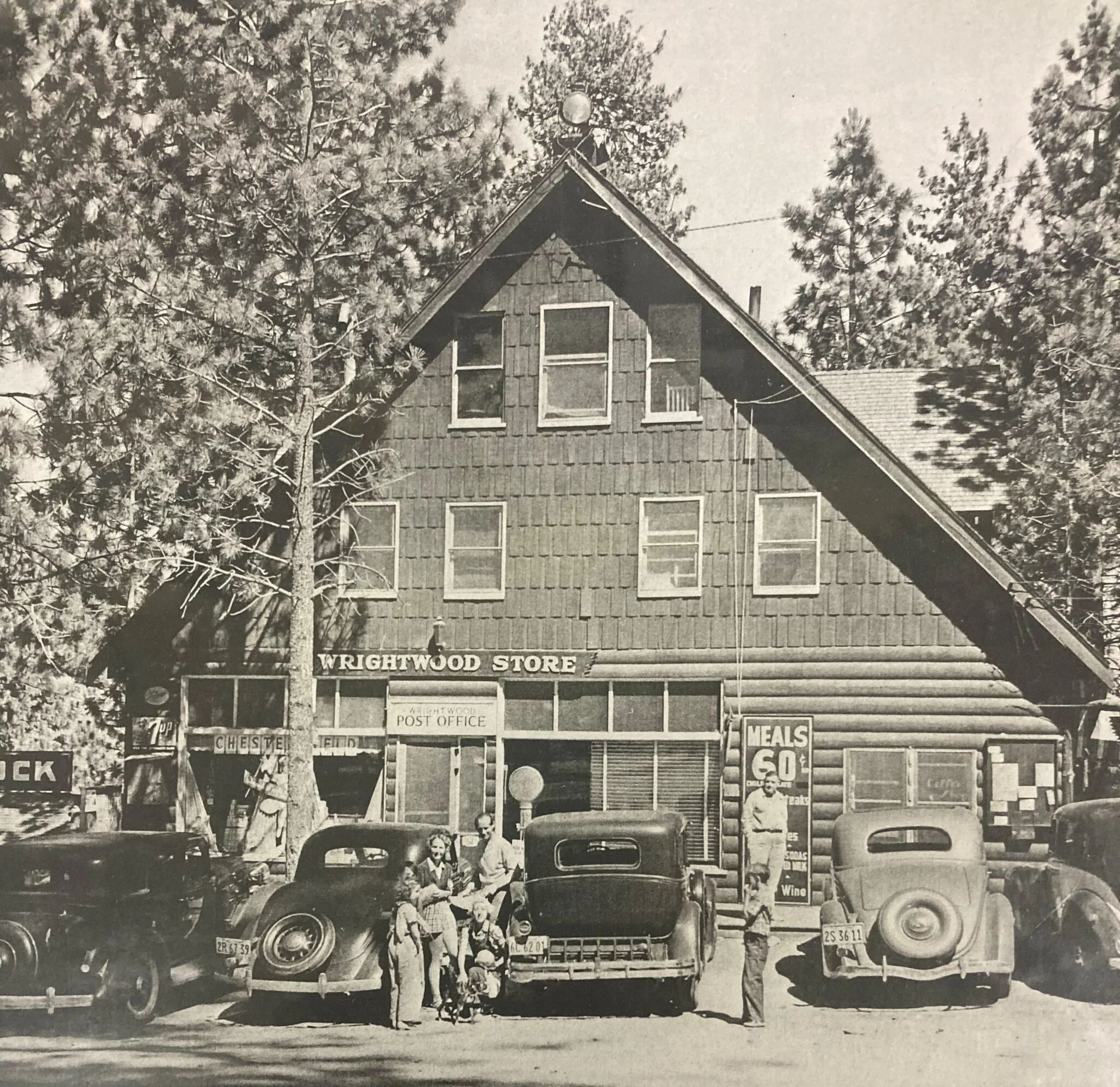Vintage photo of Wrightwood Store, a rustic wooden building with a post office sign. Classic cars and a group of people stand in front, evoking a nostalgic feel.