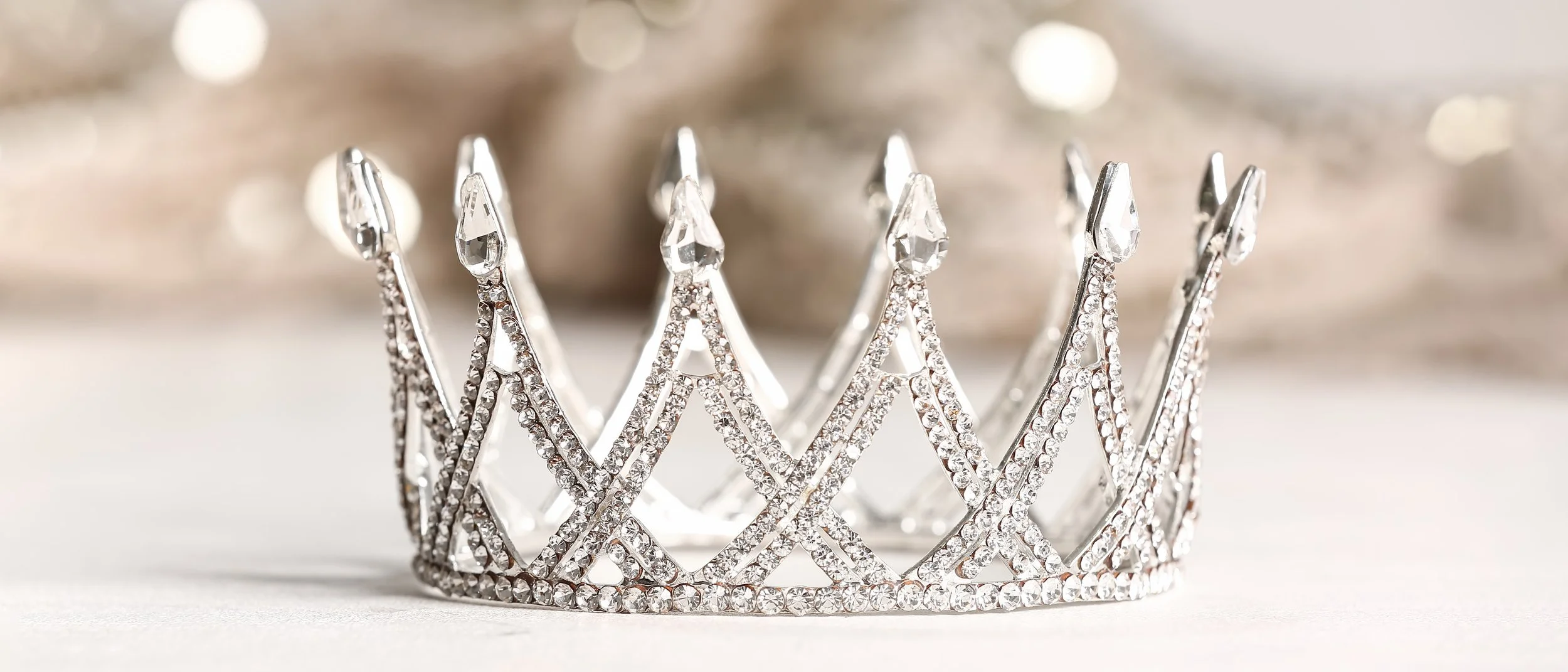 A sparkling silver tiara decorated with diamonds and intricate openwork design, placed on a light surface.
