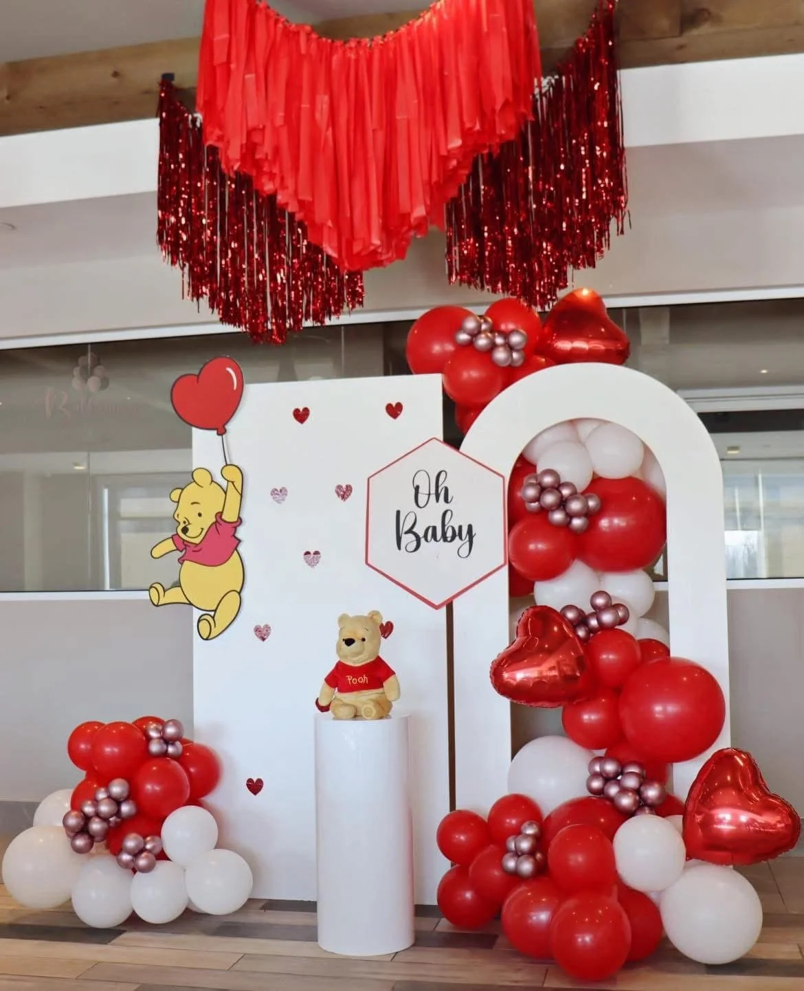 Valentine's Day themed decoration with red, white, and pink balloons, Winnie the Pooh and animal figures, and a sign that says "Oh Baby."
