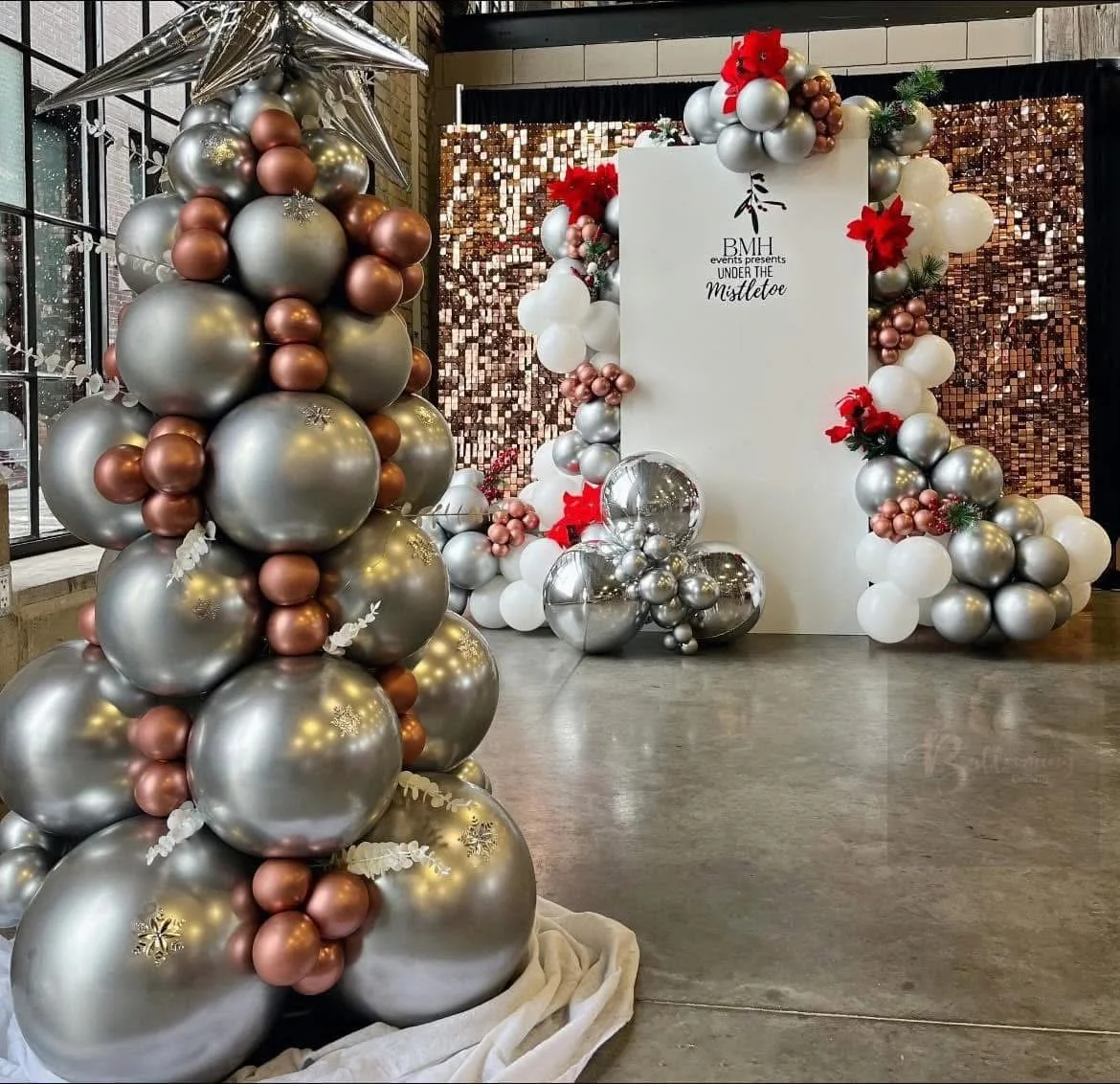 Decorative holiday balloons and backdrop for an event, with a sign reading 'BMI events presents UNDER THE Mistletoe'.
