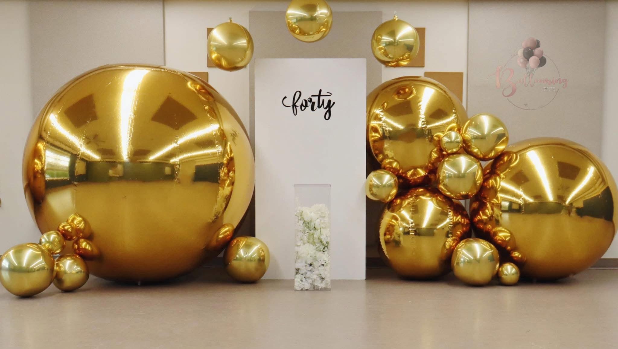 Decorative balloons in various sizes with a gold metallic finish, arranged around a white stand with 