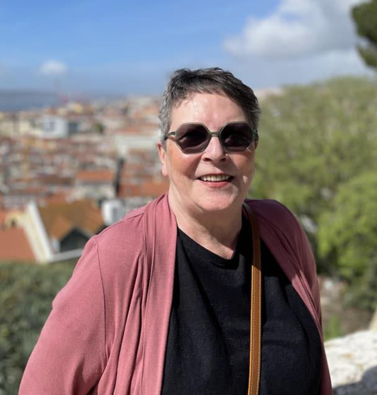 Profielfoto van Celine Willems met zonnebril, glimlachend, met een stad op de achtergrond.