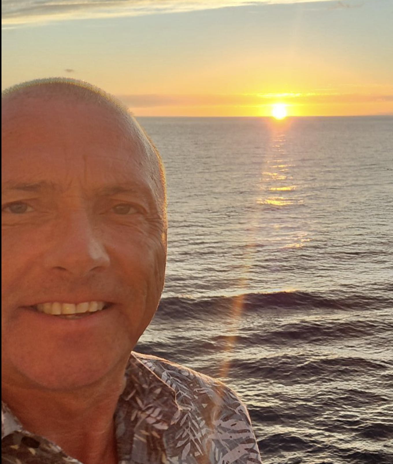Selfie van Gerry Vanderhoven aan zee bij zonsondergang, met de zon laag boven het water.