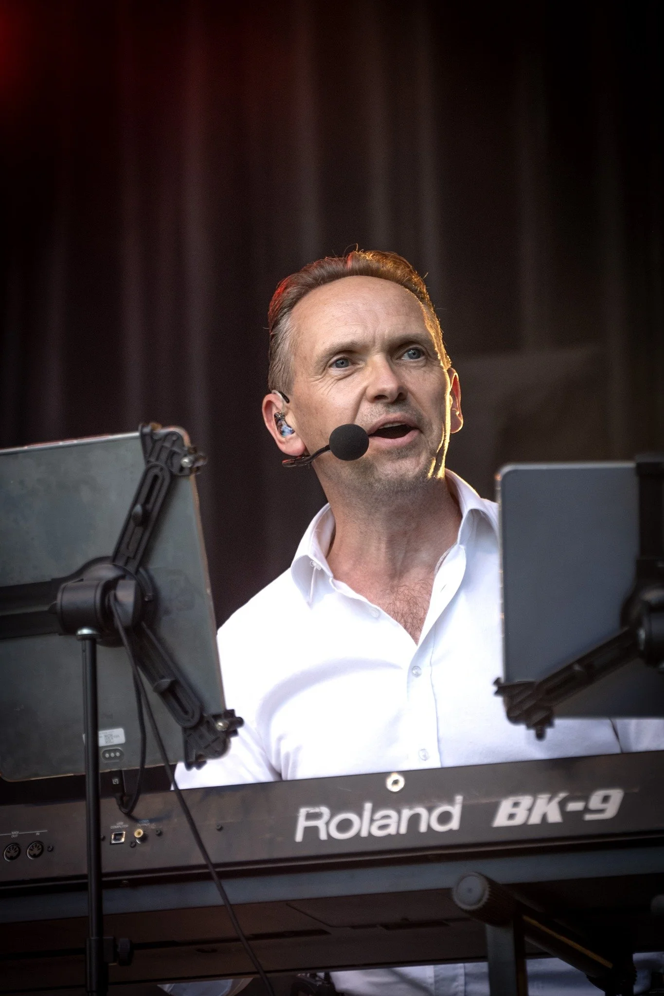 Jorgen van Whenever speelt live keyboard met headsetmicrofoon, in een wit hemd, op het podium achter een Roland-keyboard.