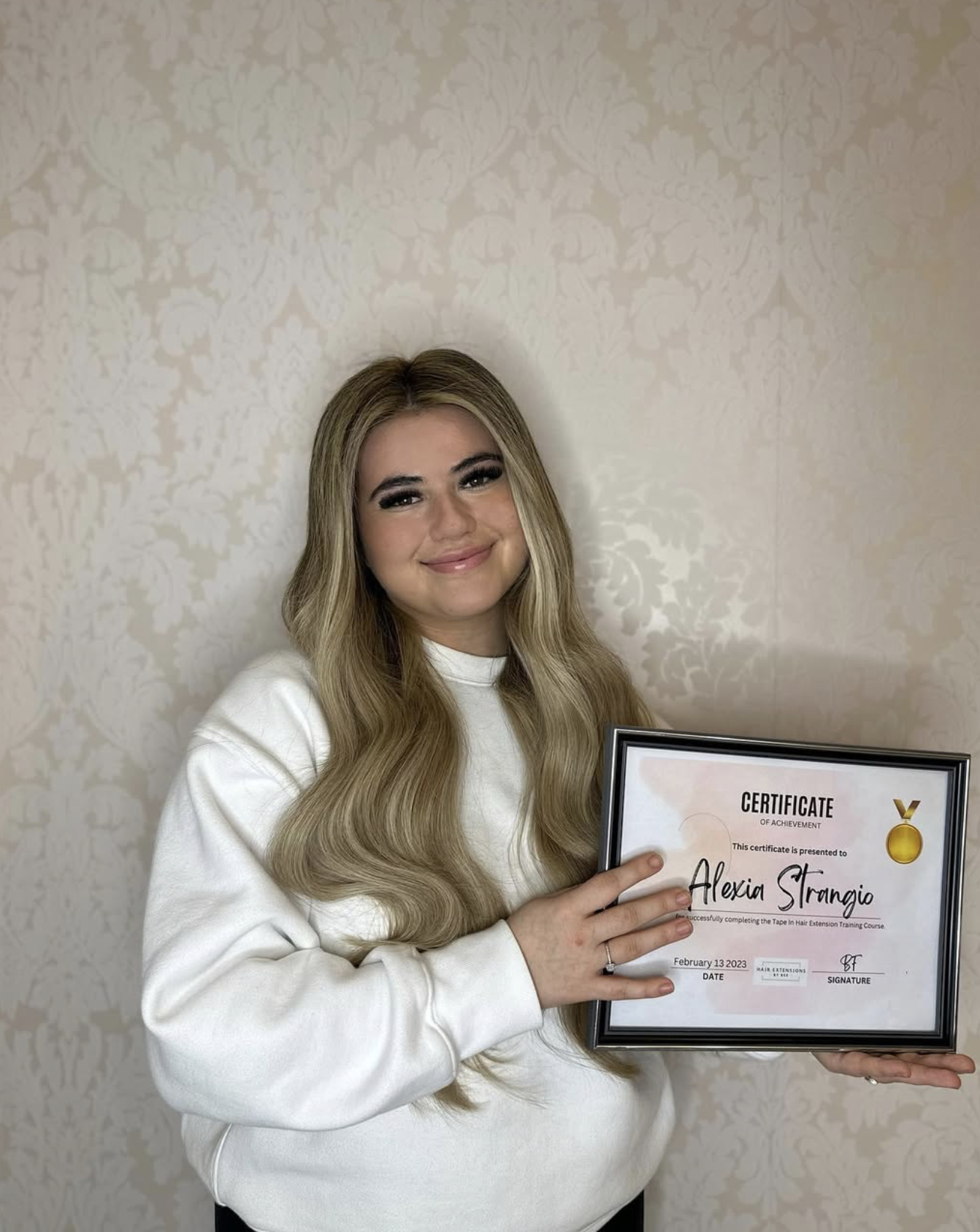 A woman with long wavy blonde hair smiling and holding a framed certificate of achievement.