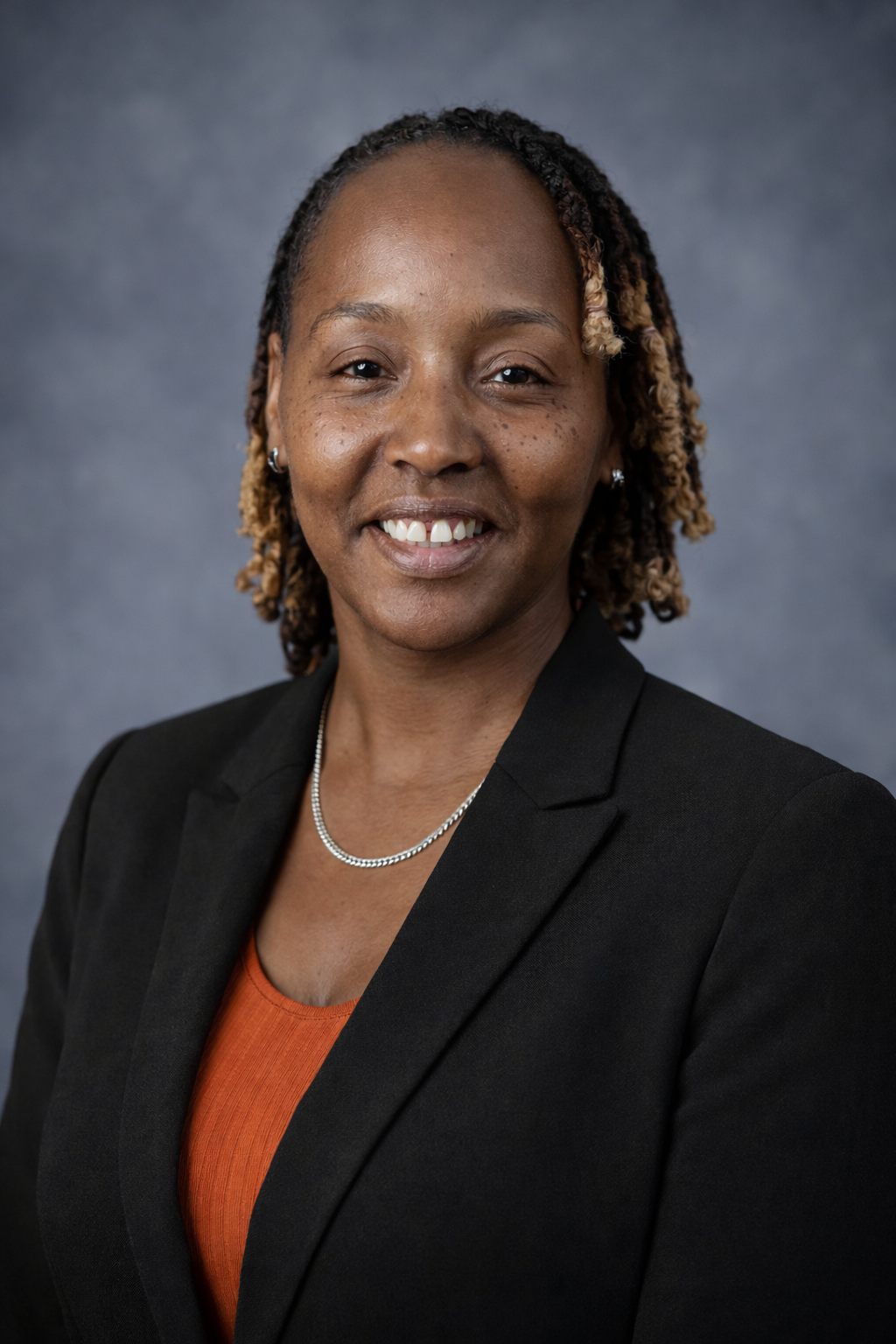 Close-up of a woman with styled hair, smiling, wearing earrings and a patterned top.