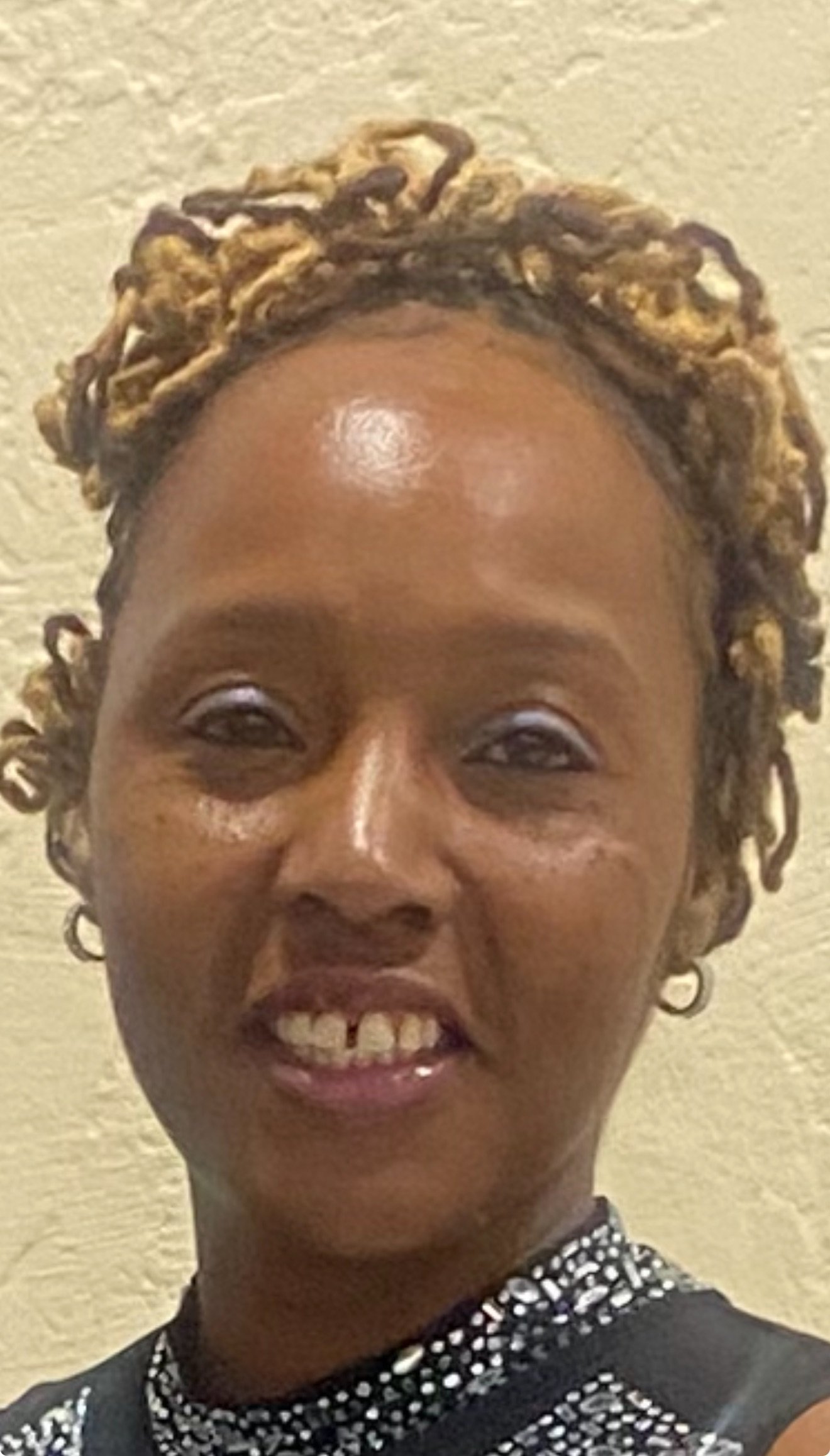 Close-up of a woman with styled hair, smiling, wearing earrings and a patterned top.