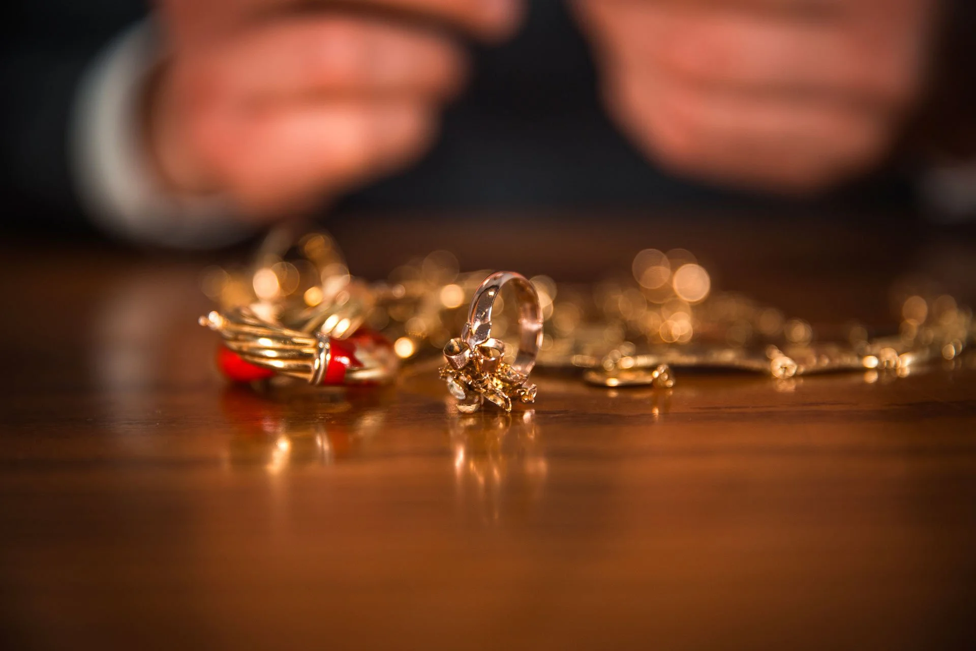 Gioielli in oro con una pietra rossa su un tavolo di legno, mani sullo sfondo