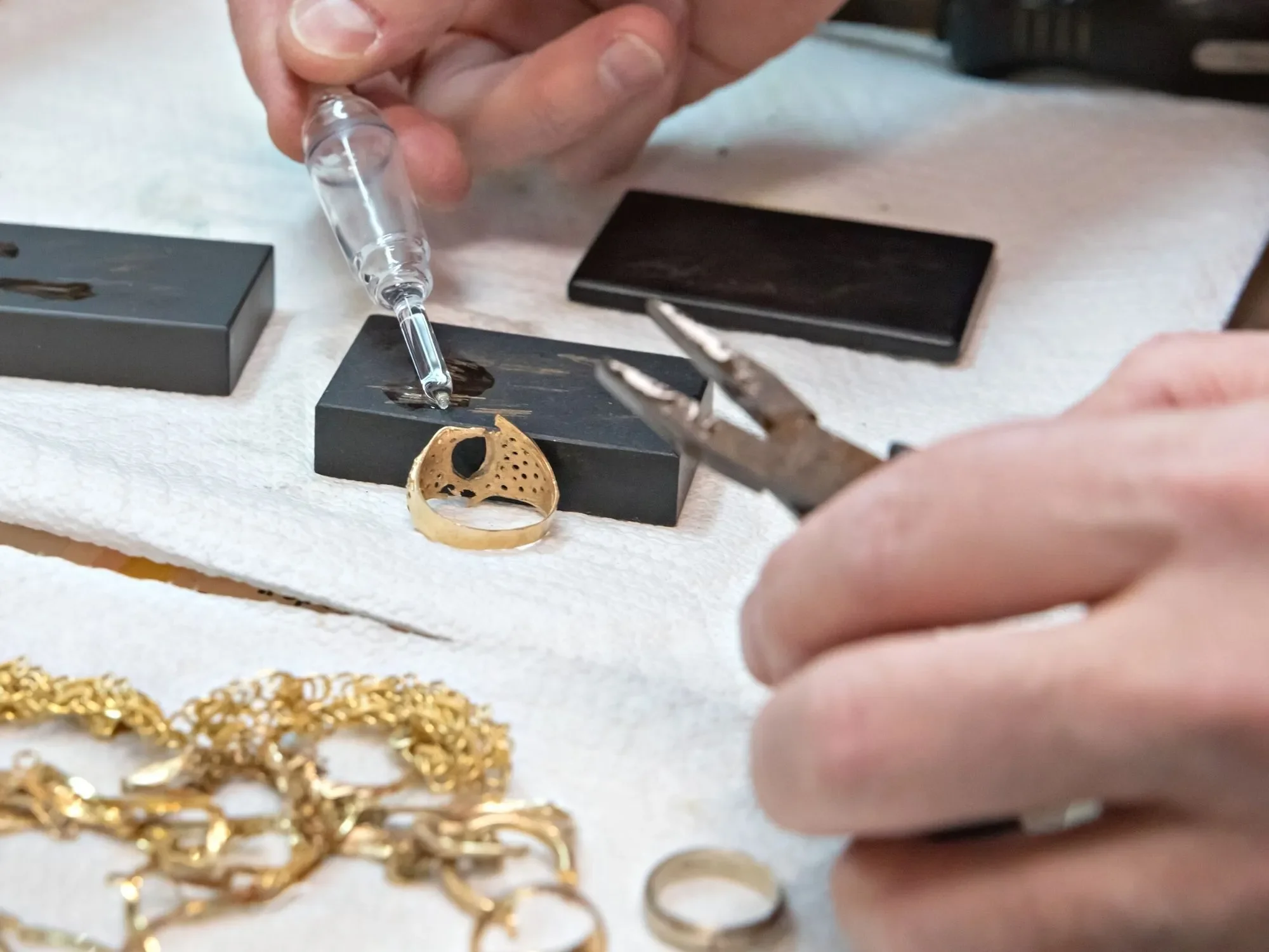 Mani che verificano un anello d'oro con il reagente sulla pietra di paragone, catene d'oro accanto