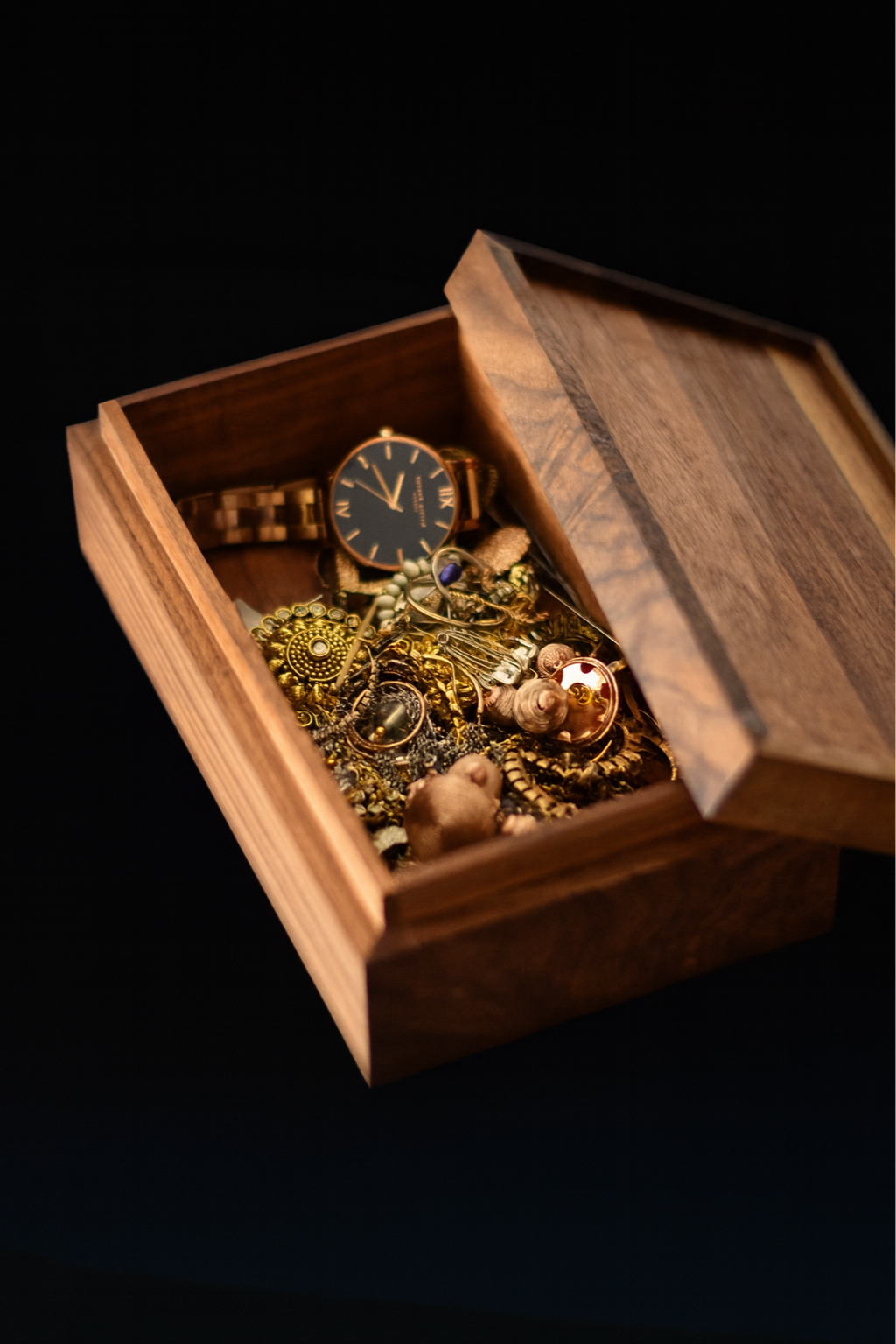 Scatola di legno aperta con gioielli e un orologio d'oro su fondo nero