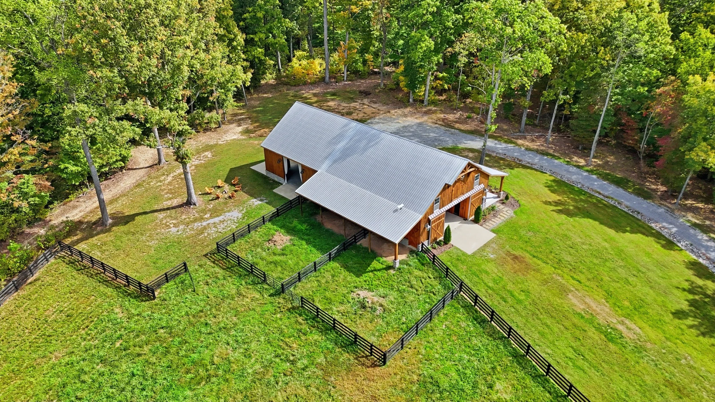 A wooden barn-style building with an overhang, surrounded by green grass and trees, under a partly cloudy sky.