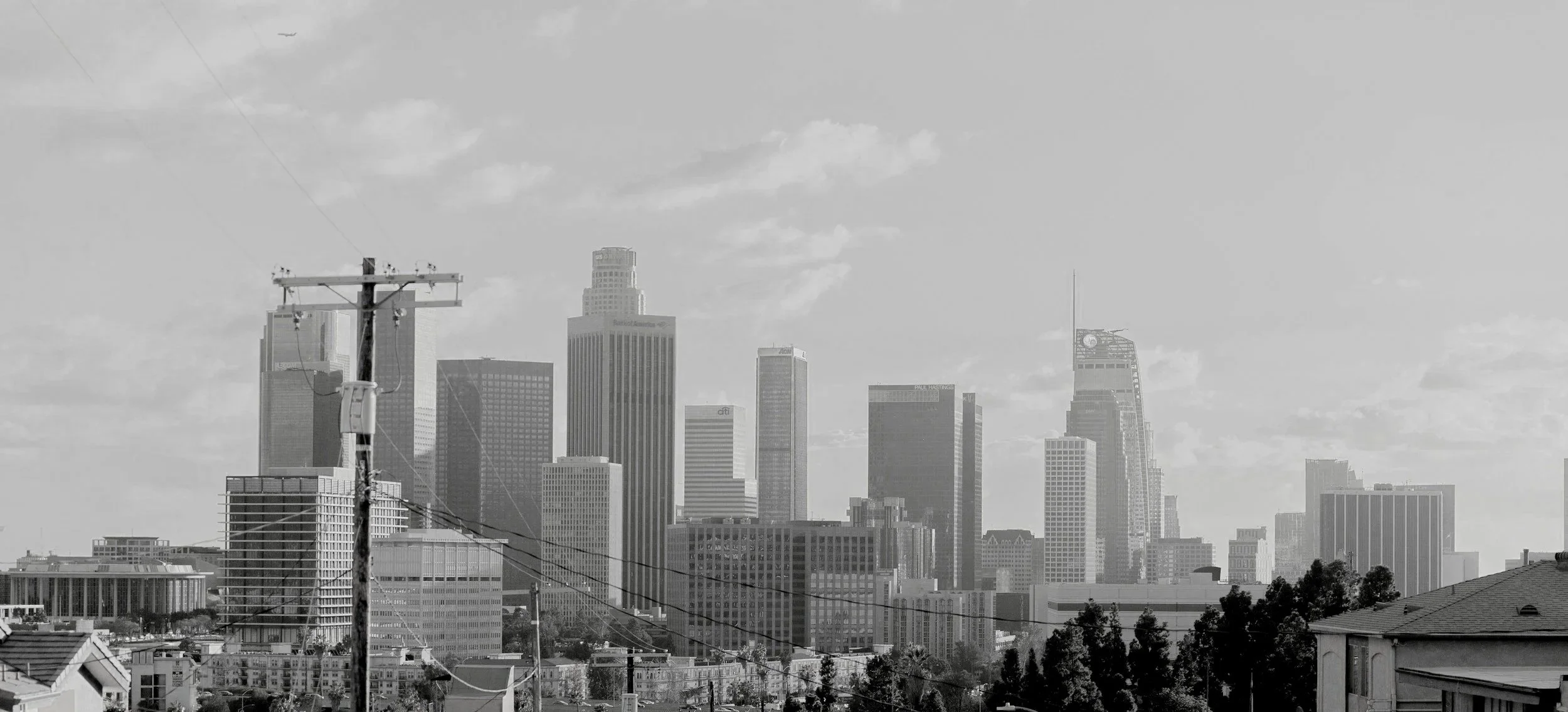 Black and white photo of the downtown Los Angeles skyline with tall skyscrapers and a utility pole in the foreground.