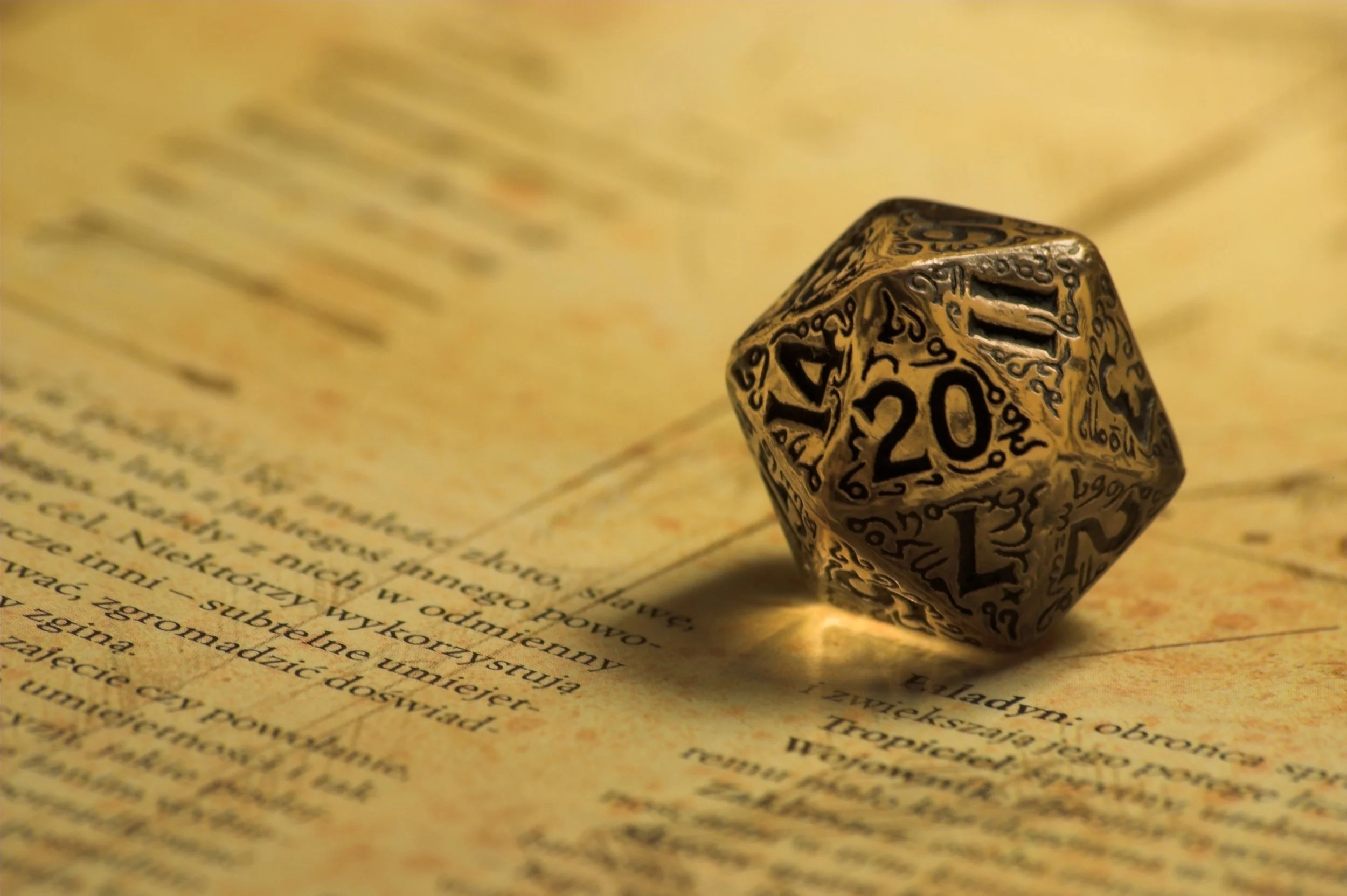 A 20-sided metallic die with intricate black decorative patterns resting on an open book with yellowed pages.