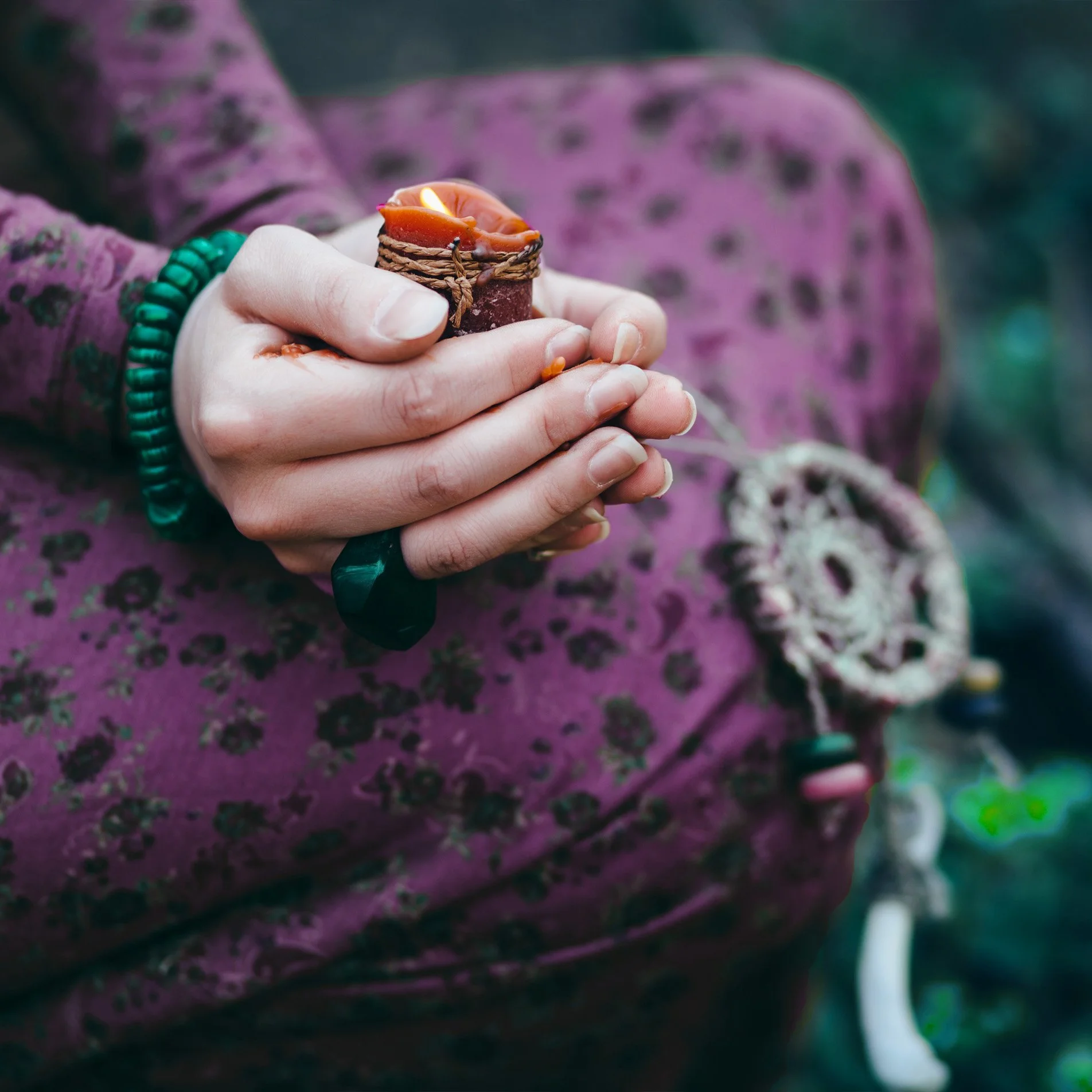 Mano sosteniendo una vela encendida con cinturón y accesorios en un entorno natural.