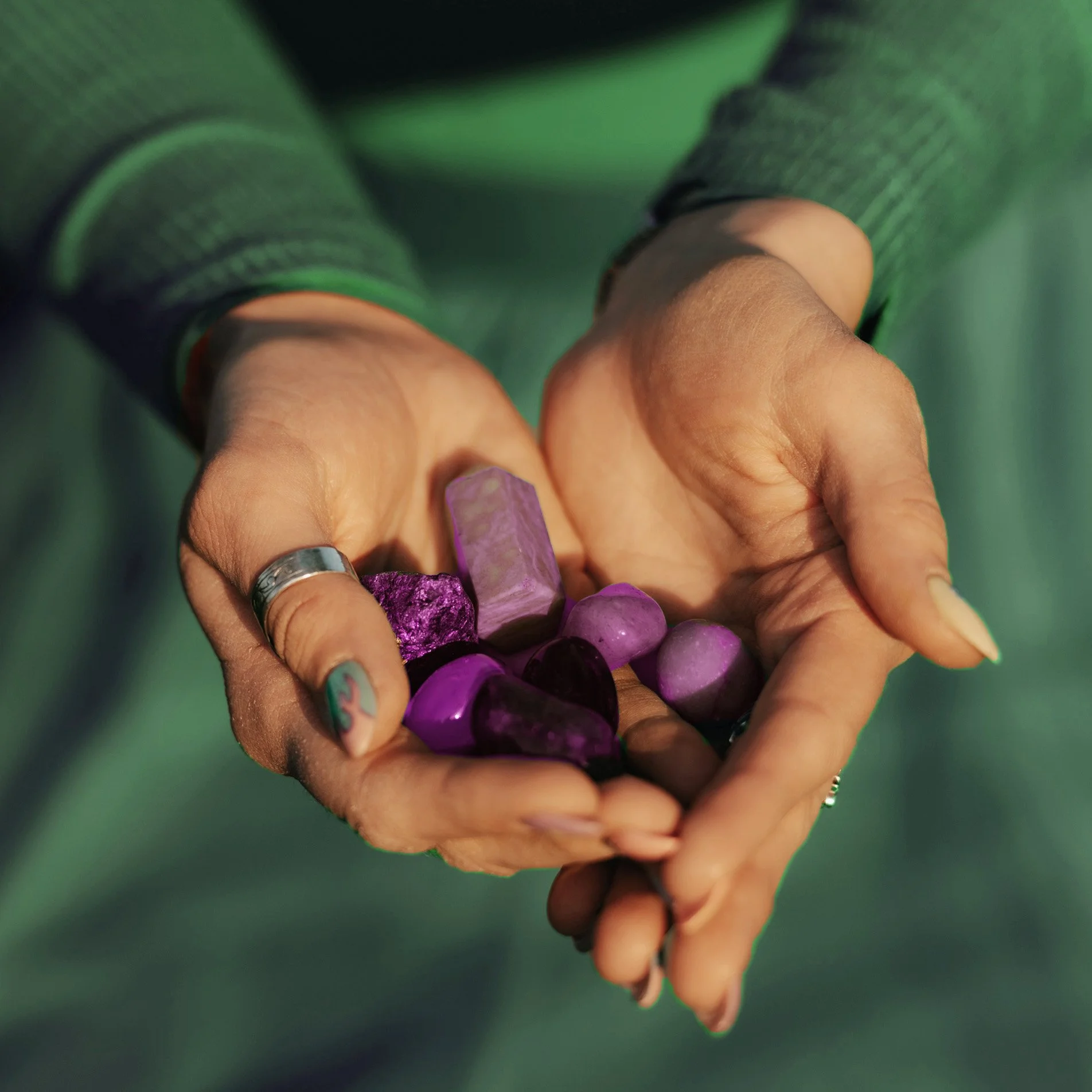 Manos sosteniendo varias piedras y cristales morados y lilas, algunas pulidas y otras con textura.