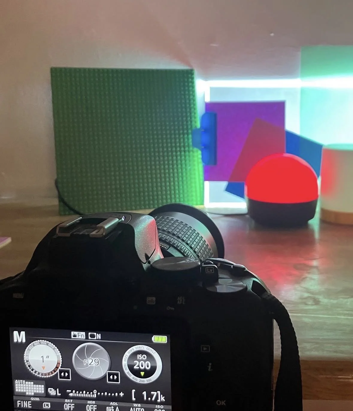 Photograph of a camera's viewfinder screen showing camera settings, with colorful LED lights, a green Lego structure, and a spherical red and black object in the background.