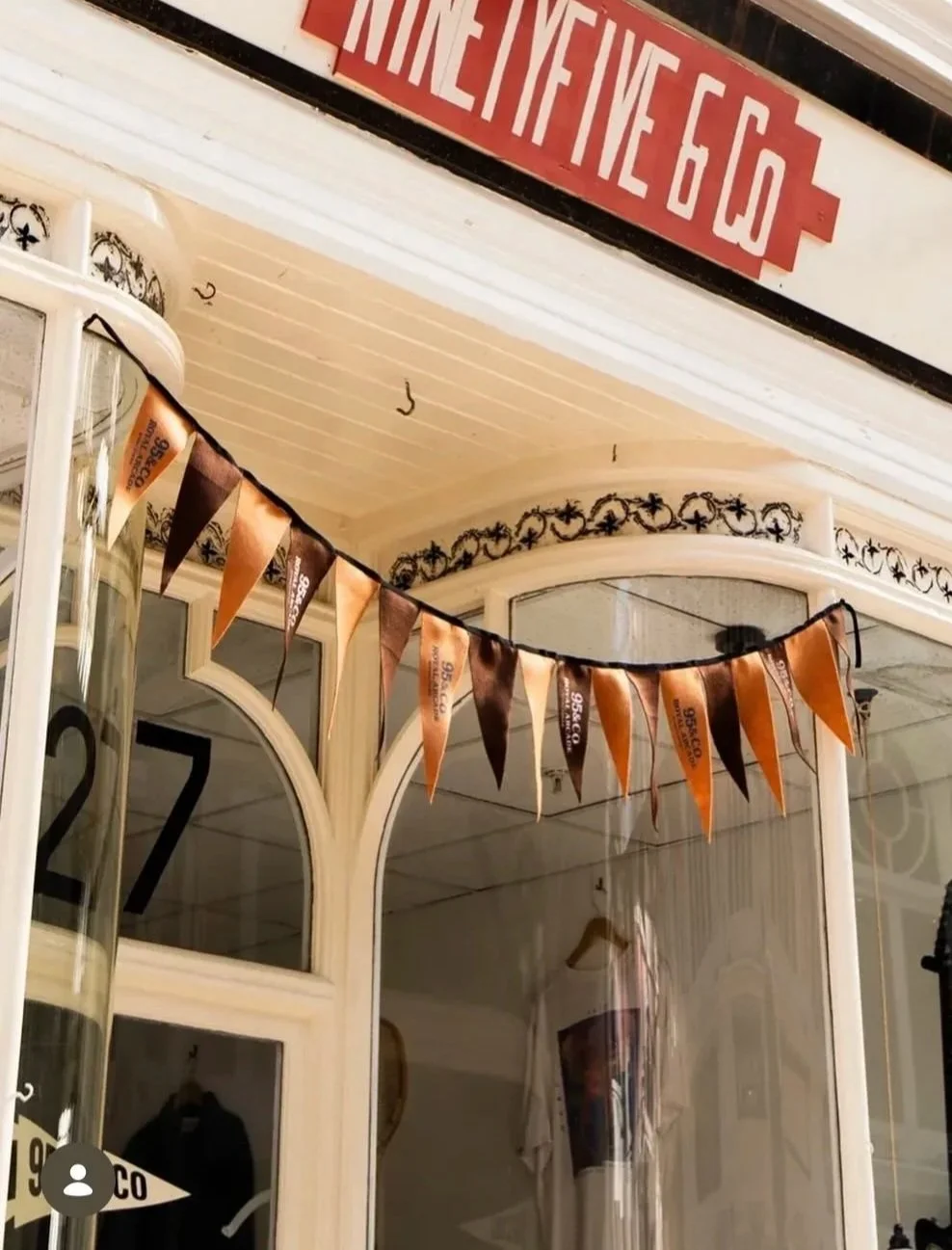 A decorated storefront with a string of orange and brown pennant flags and a red sign with white lettering