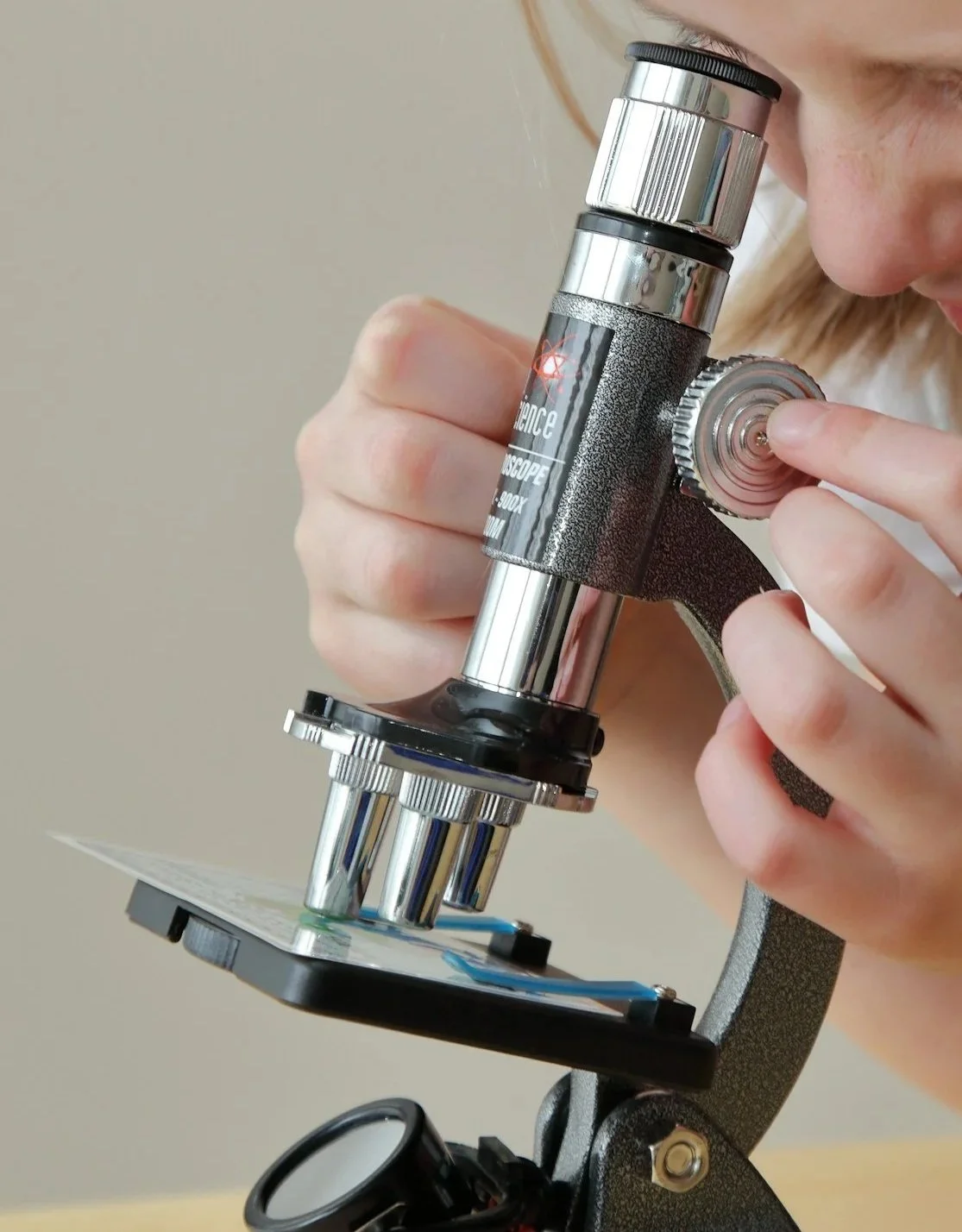Person looking through a microscope with a black and silver body, focusing on a slide placed on the stage.