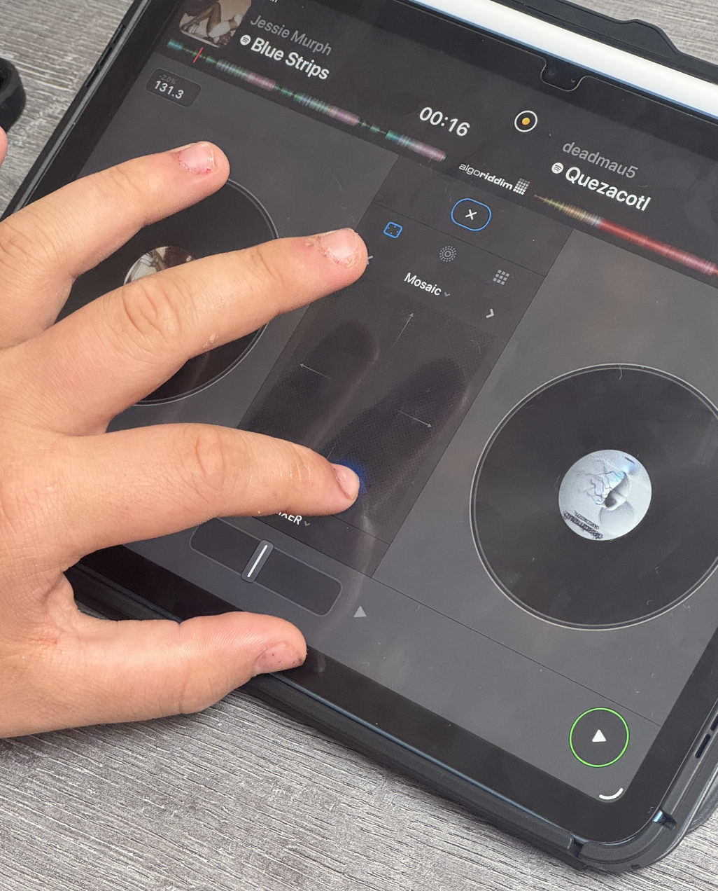 A pupil using a tablet to DJ a music playlist. The screen shows two virtual turntables, a playlist with song titles, and a waveform of the current song. The playlist includes songs titled 'Blue Strips' by Jessie Murph and others.