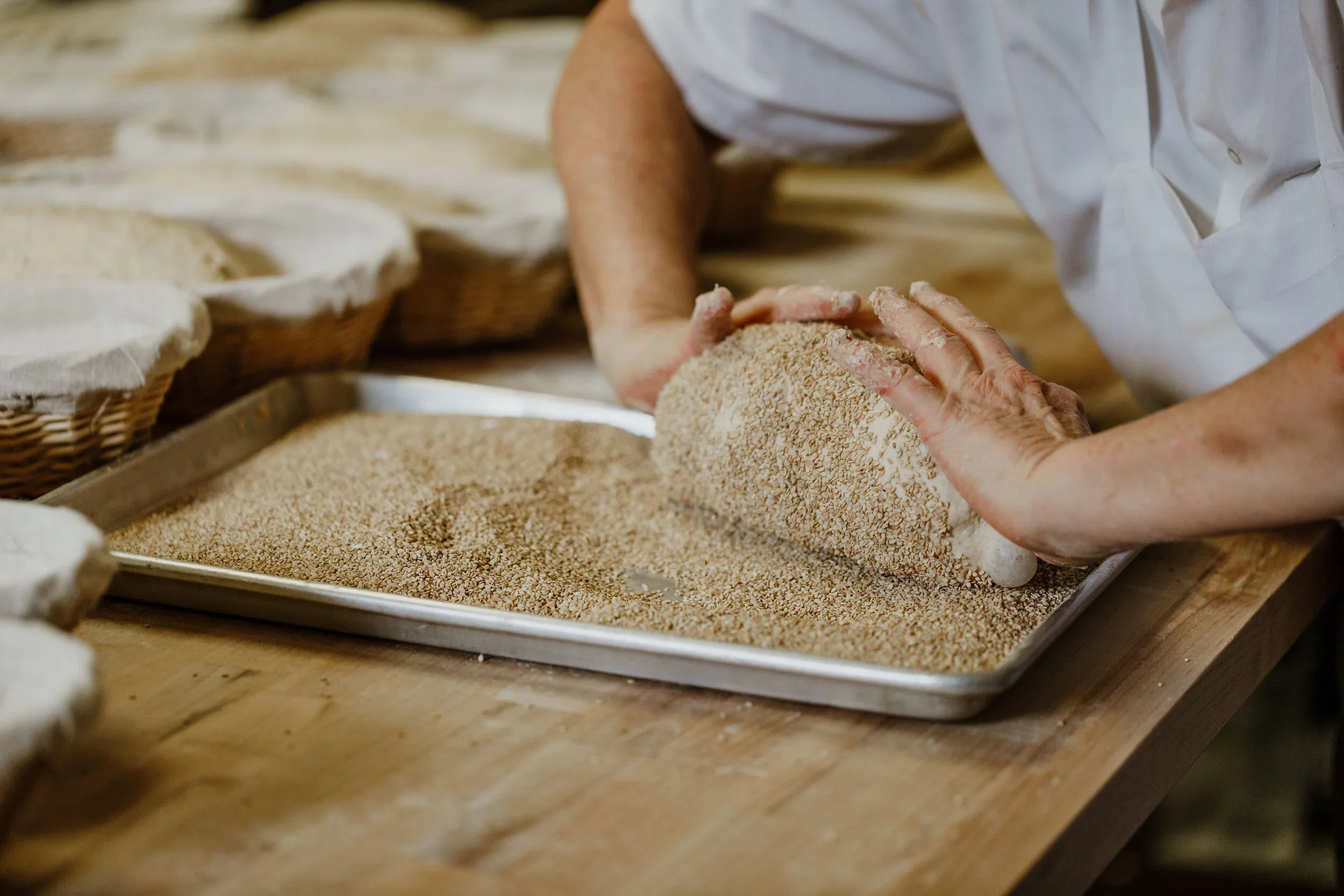 Person rolling breadcrumbs onto a baking tray in a bakery kitchen.