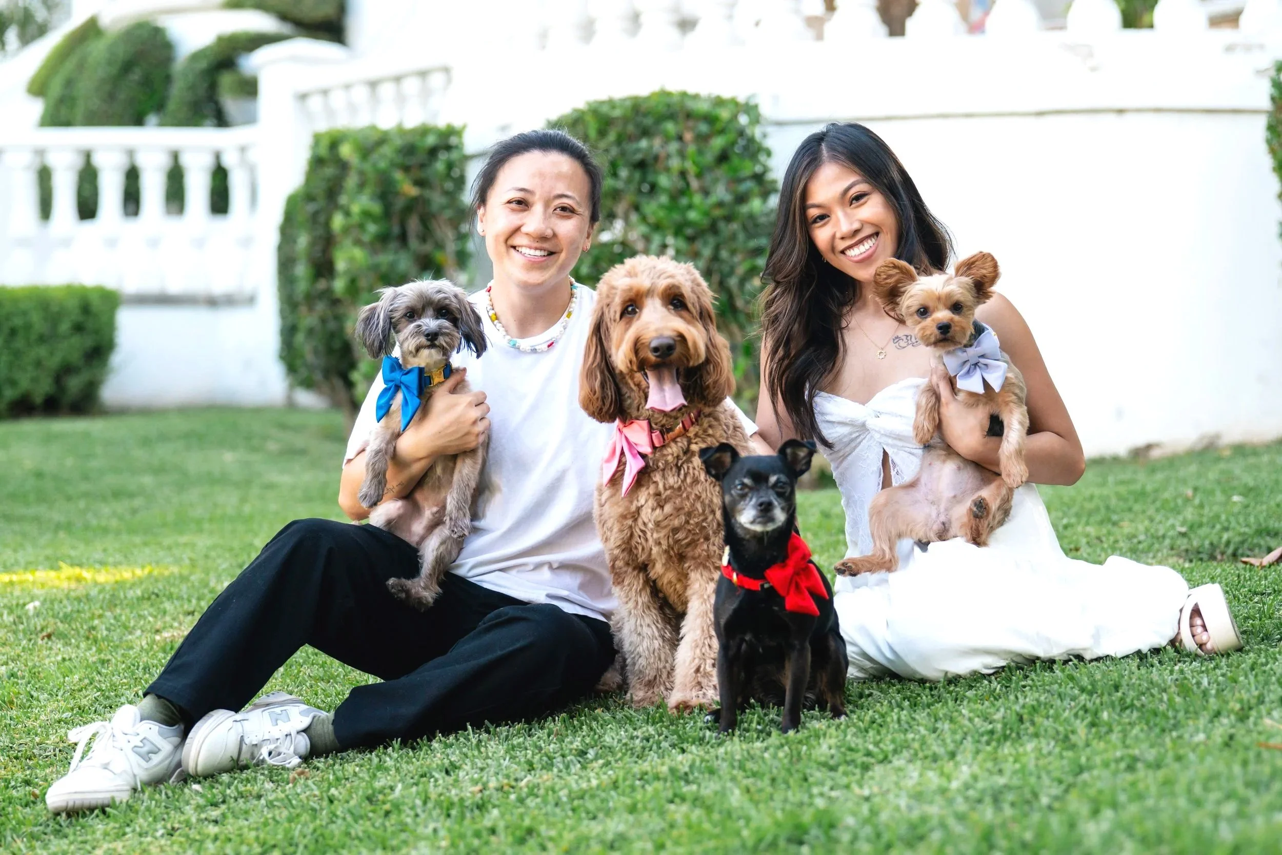 Two women with four dogs in front of a white house.