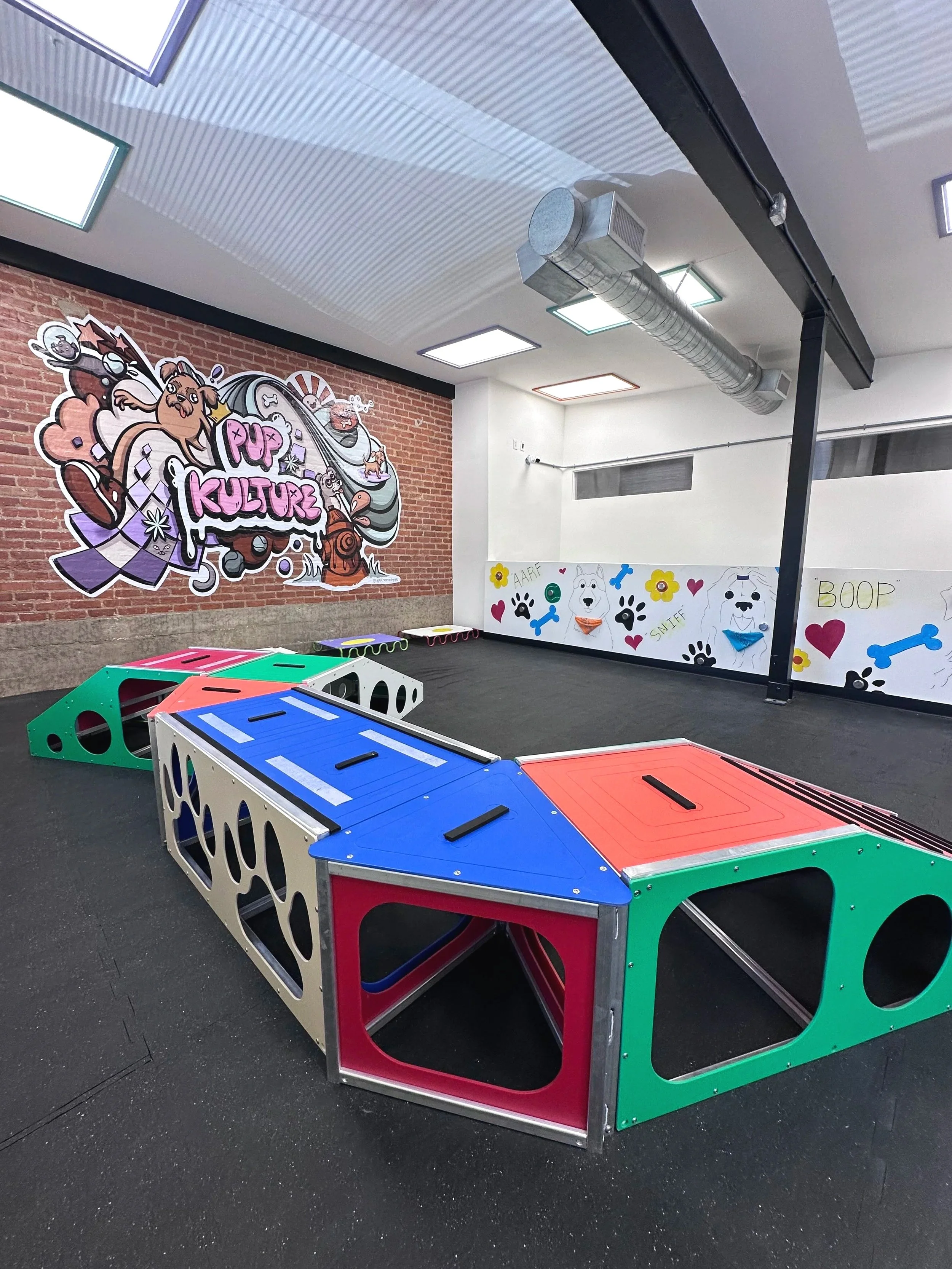Dog daycare in Pasadena with indoor playground with a colorful mural, dog play structure, and a dog sniffwall.
