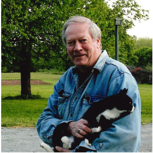 Smiling young Asian woman with short black hair in a blue top, outdoors with green foliage in the background.