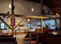 Interior of a rustic cafe with wooden beams, hanging lights, and seating area.