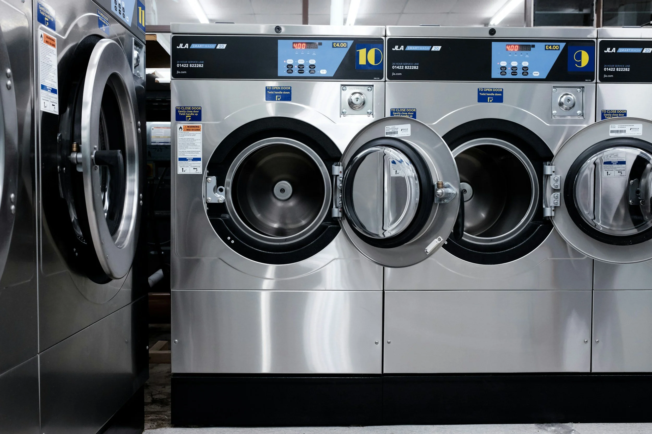 A row of industrial washing machines with open doors in a laundromat.