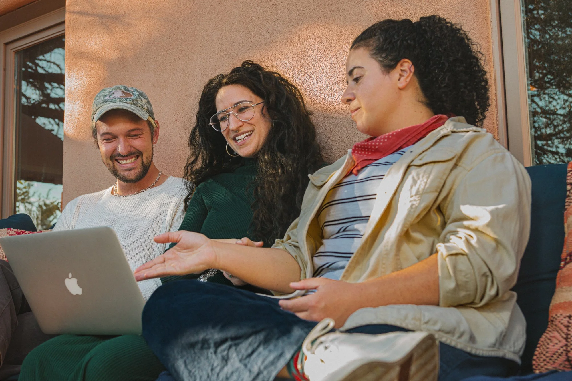 A poly group sitting on a couch outdoors, looking at a laptop together, smiling and engaging in conversation.