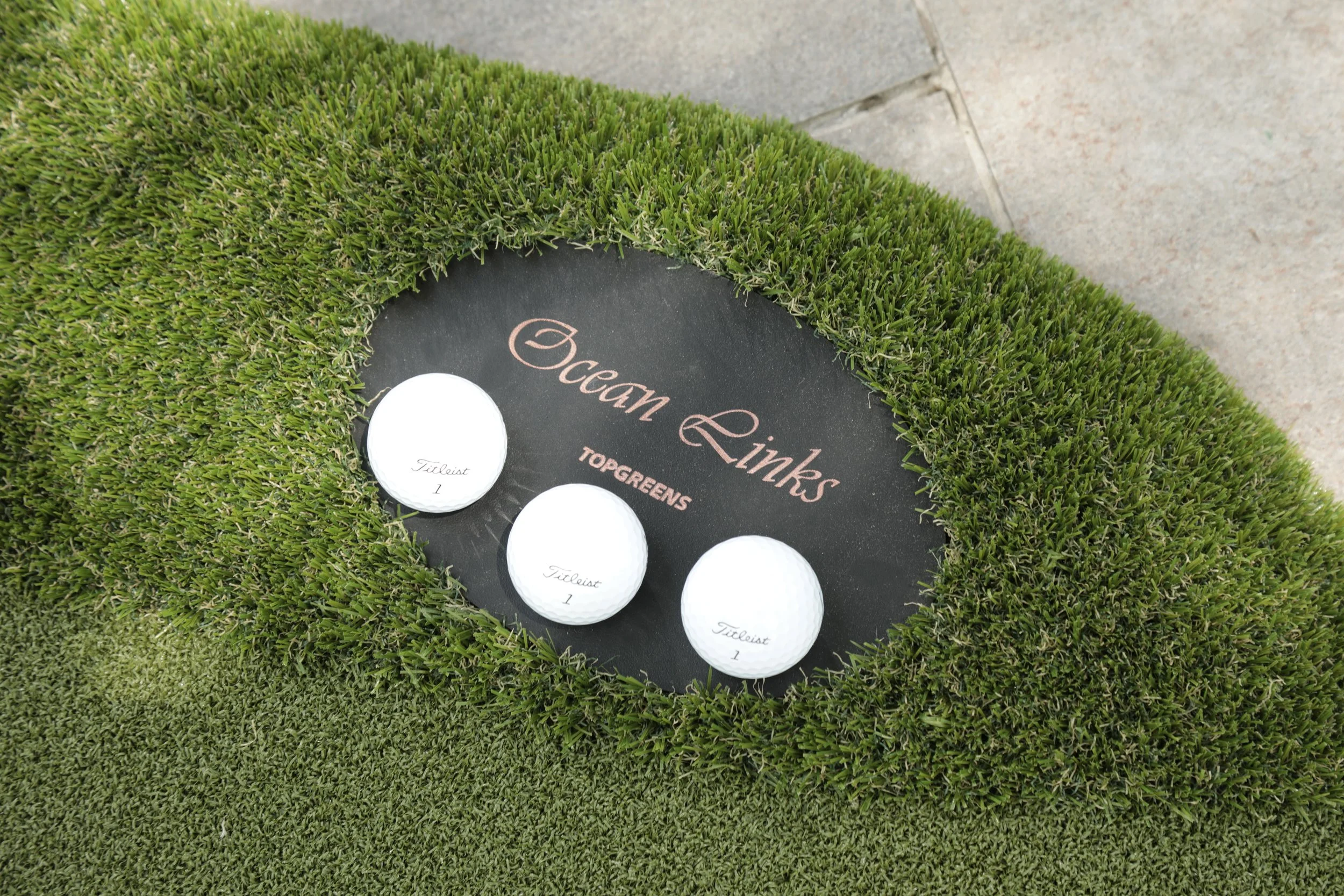 close up of a modular artifical grass putting green withthe name plaque, Ocan Links, with 3 golf calls resting on it