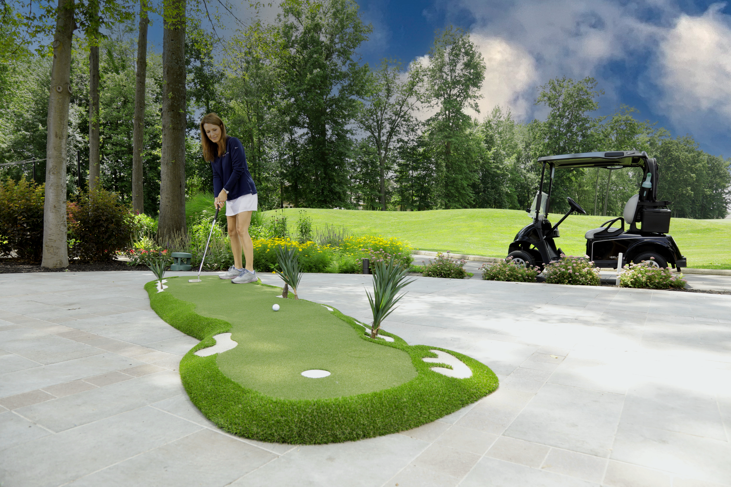 A woman playing miniature golf on a cardboard and turf course, with a golf cart parked nearby and trees in the background.