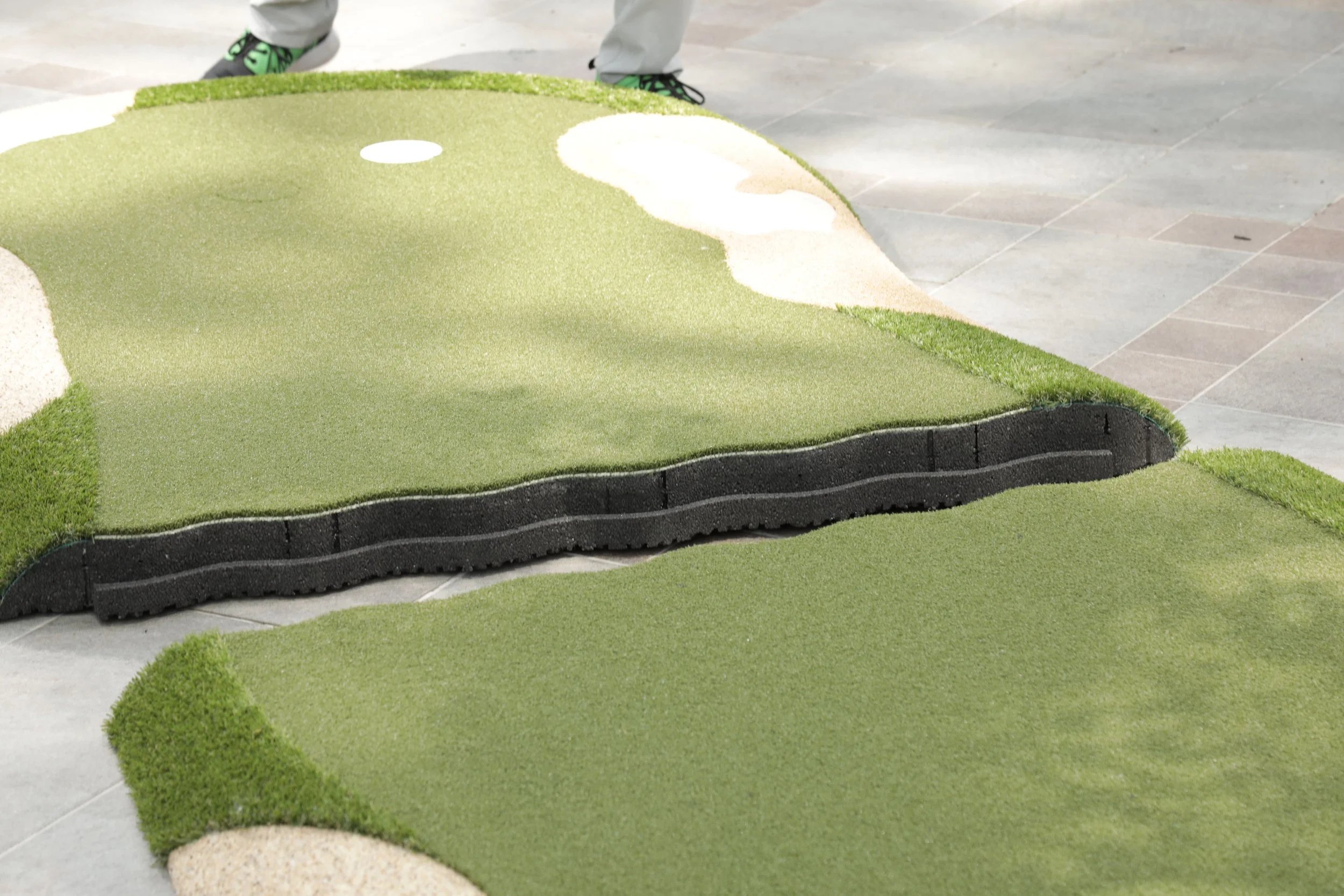 2 pieces of a portable putting green sitting a few inches apart from each other