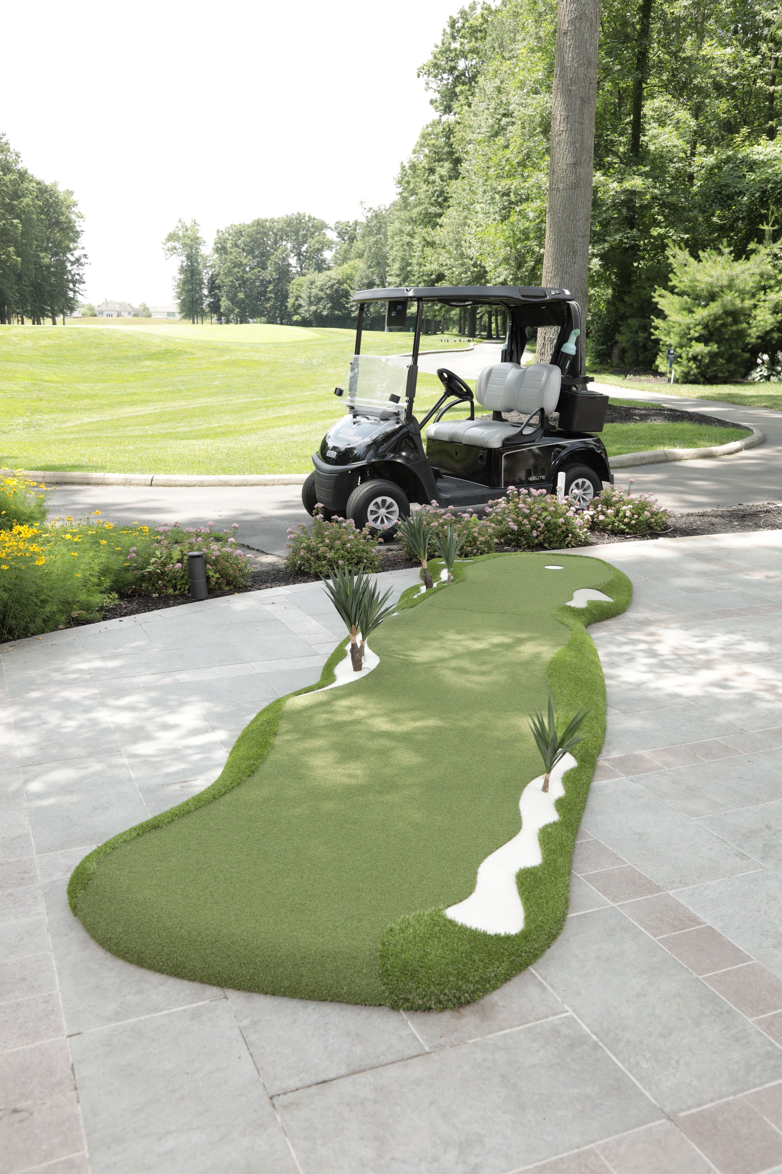 close up of an artifical grass modular putting green that has artifiical tropic trees on it with a golf cart in the background