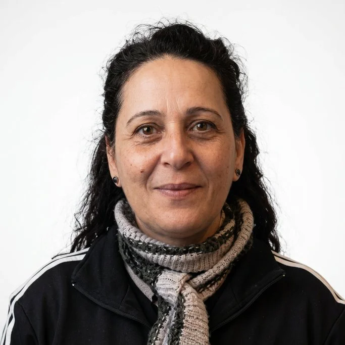 A woman with dark curly hair wearing a black jacket with white stripes and a gray scarf, standing against a plain white background.