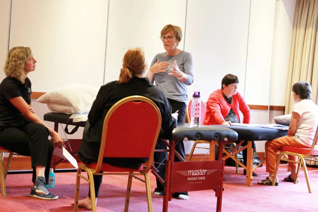 Four women and a therapist in a therapy session, with a massage table in the room.