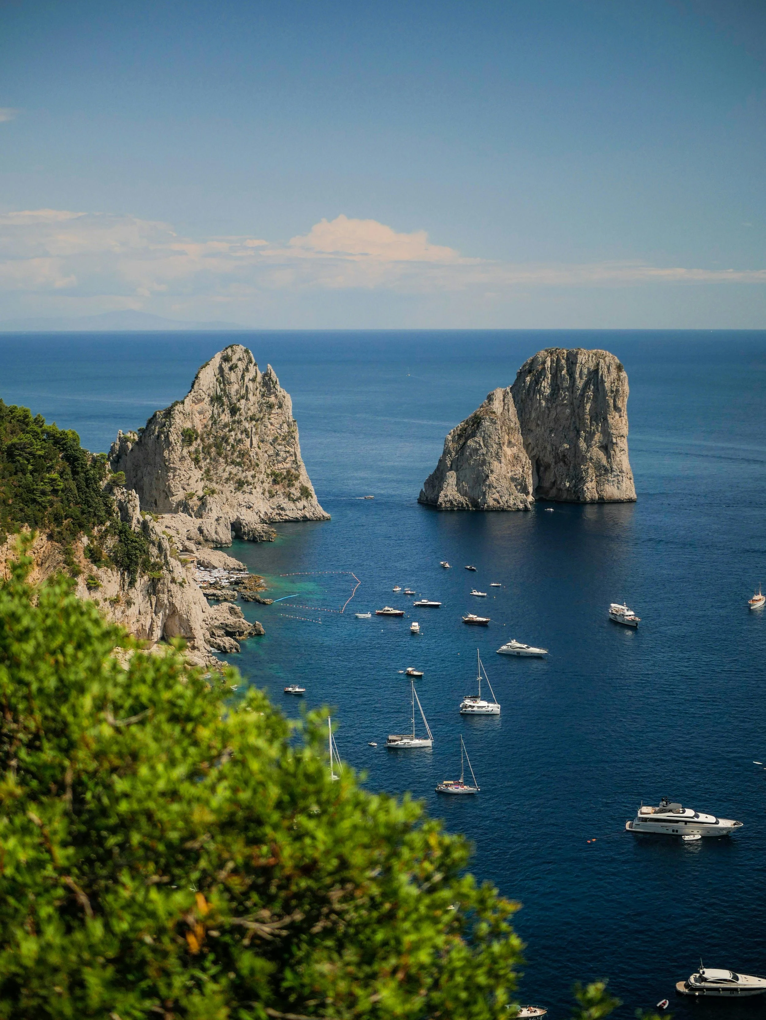 A coastal scene with large rocky cliffs, a blue sea, and several boats anchored near the coast.