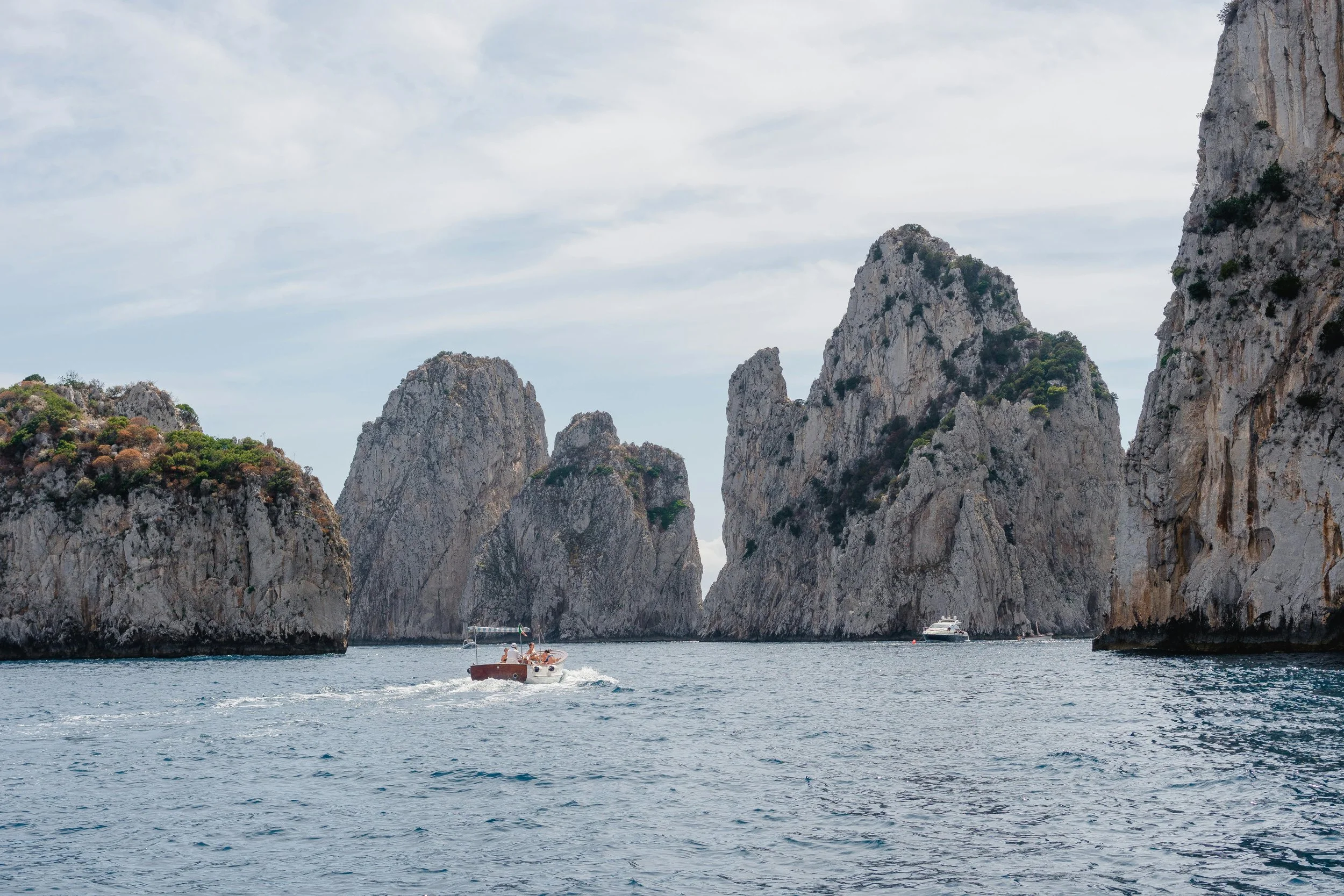 A scenic view of a rocky coastal area with tall limestone cliffs and a boat on the water. Capri, Italy.