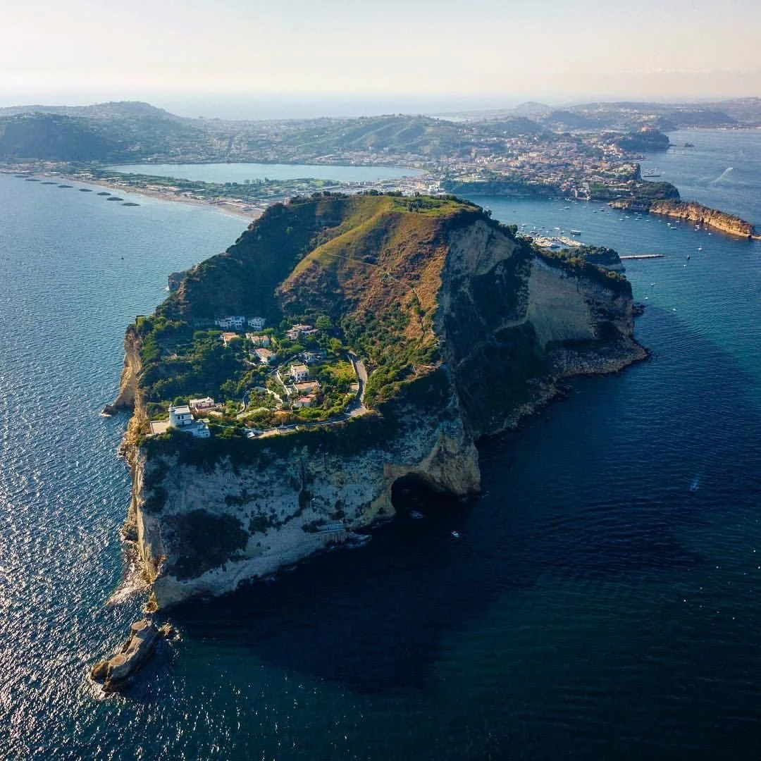 Aerial view of a large rocky island with green vegetation and some buildings on top, surrounded by deep blue ocean water.