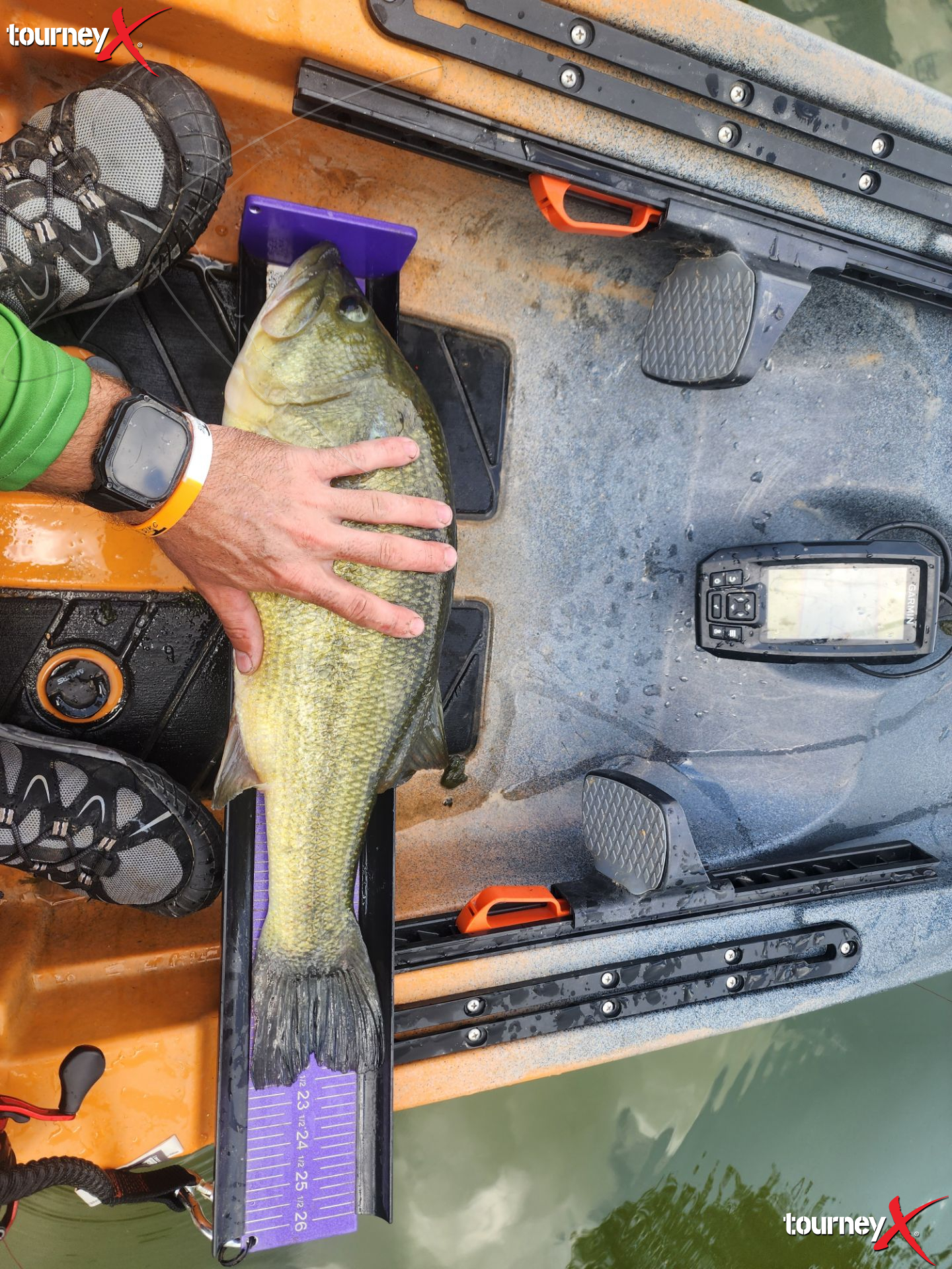 A person holding a large fish on a measuring board on a boat, with fishing equipment around, including a GPS device, and water in the background.