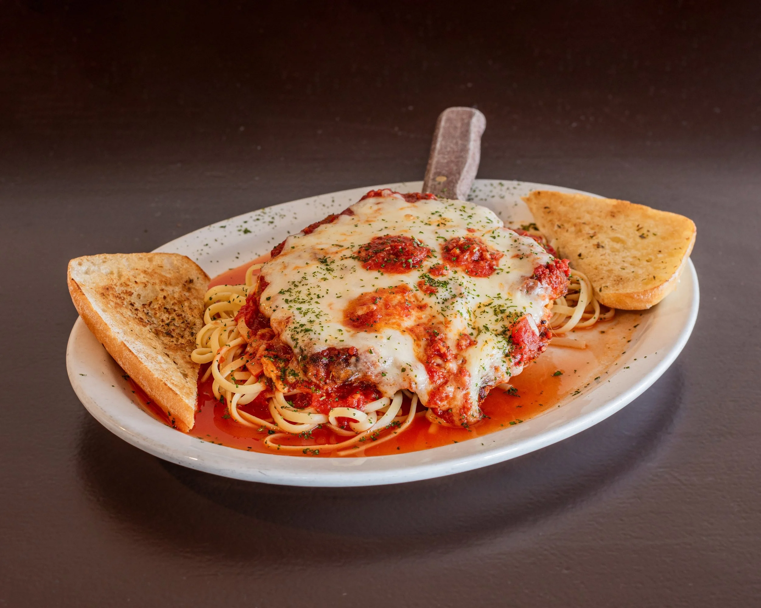 Plate with chicken cutlet and spaghetti with melted cheese and tomato sauce, garnished with herbs, served with garlic bread slices.