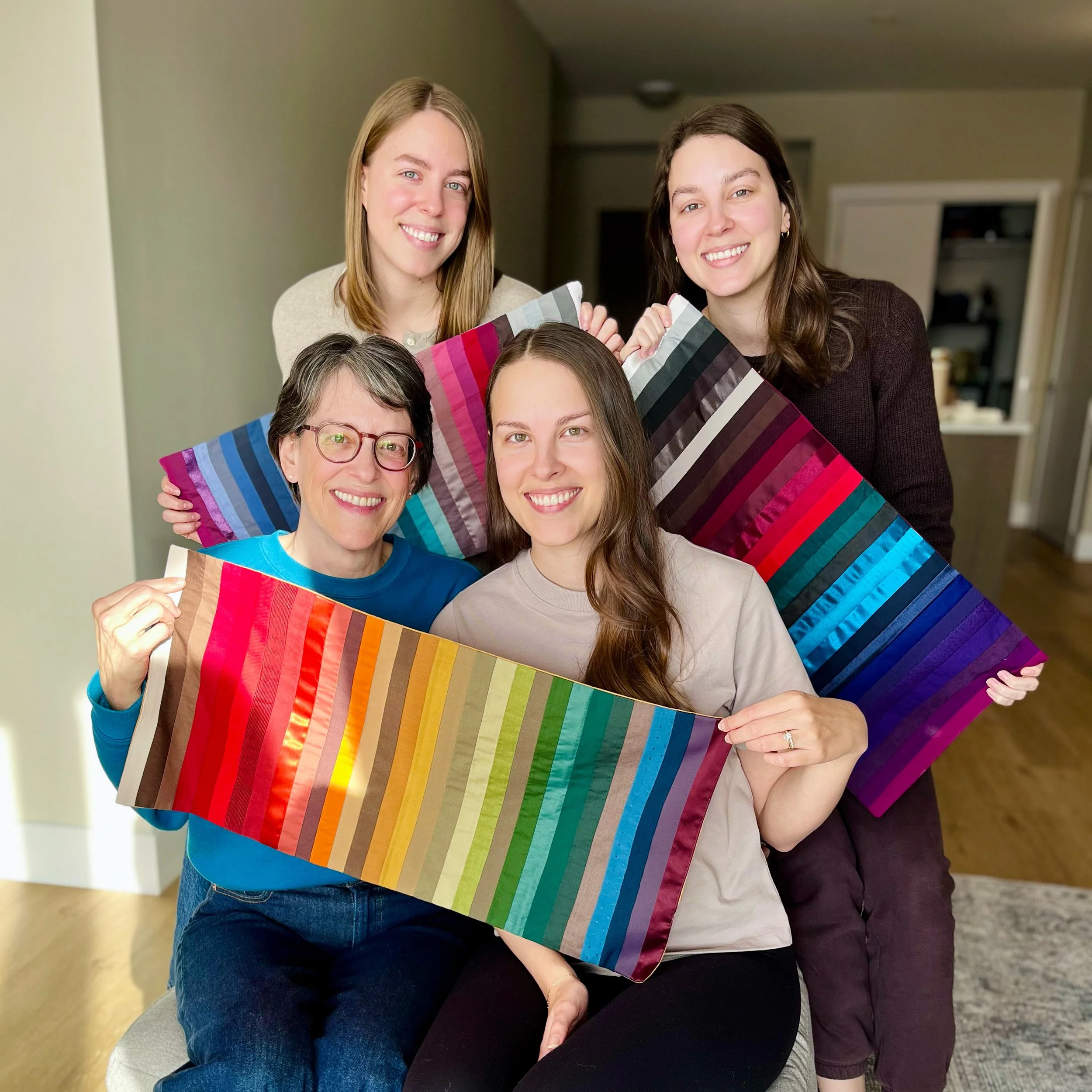 Four women smiling and holding color swatches of various shades, standing inside a home.