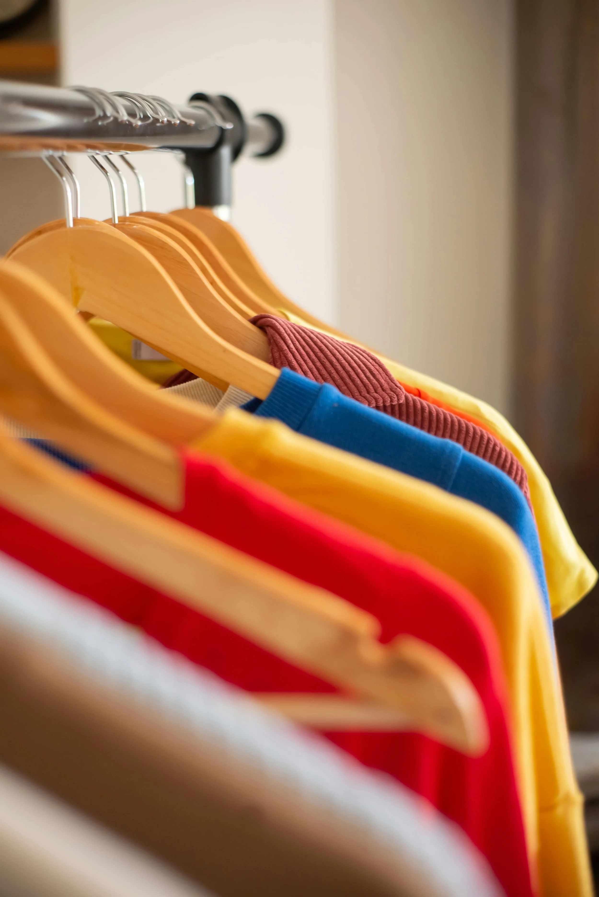 Colorful T-shirts hanging on wooden and plastic hangers on a metal clothing rack.