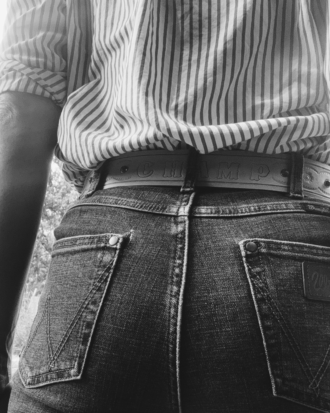 Close-up of a person wearing a striped shirt tucked into high-waisted jeans with a belt.