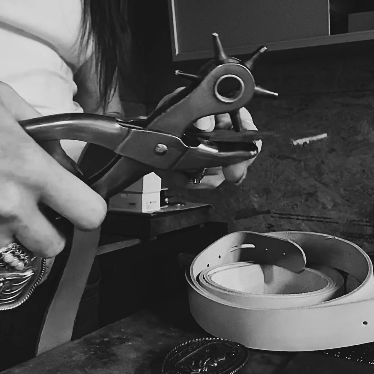 A person is using pliers on a belt and a waffle iron on a wooden table.