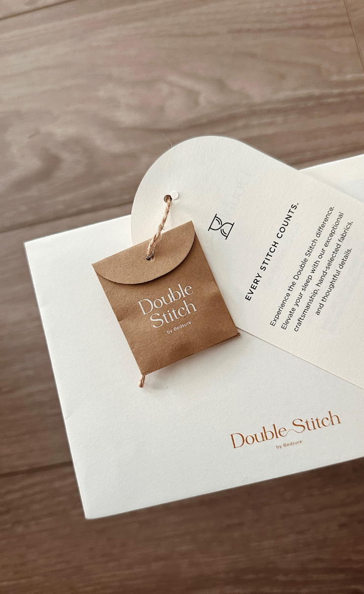 Close-up of a white box with a brown tag reading "Double Stitch by Bedsure" attached with a string, resting on a wooden surface.