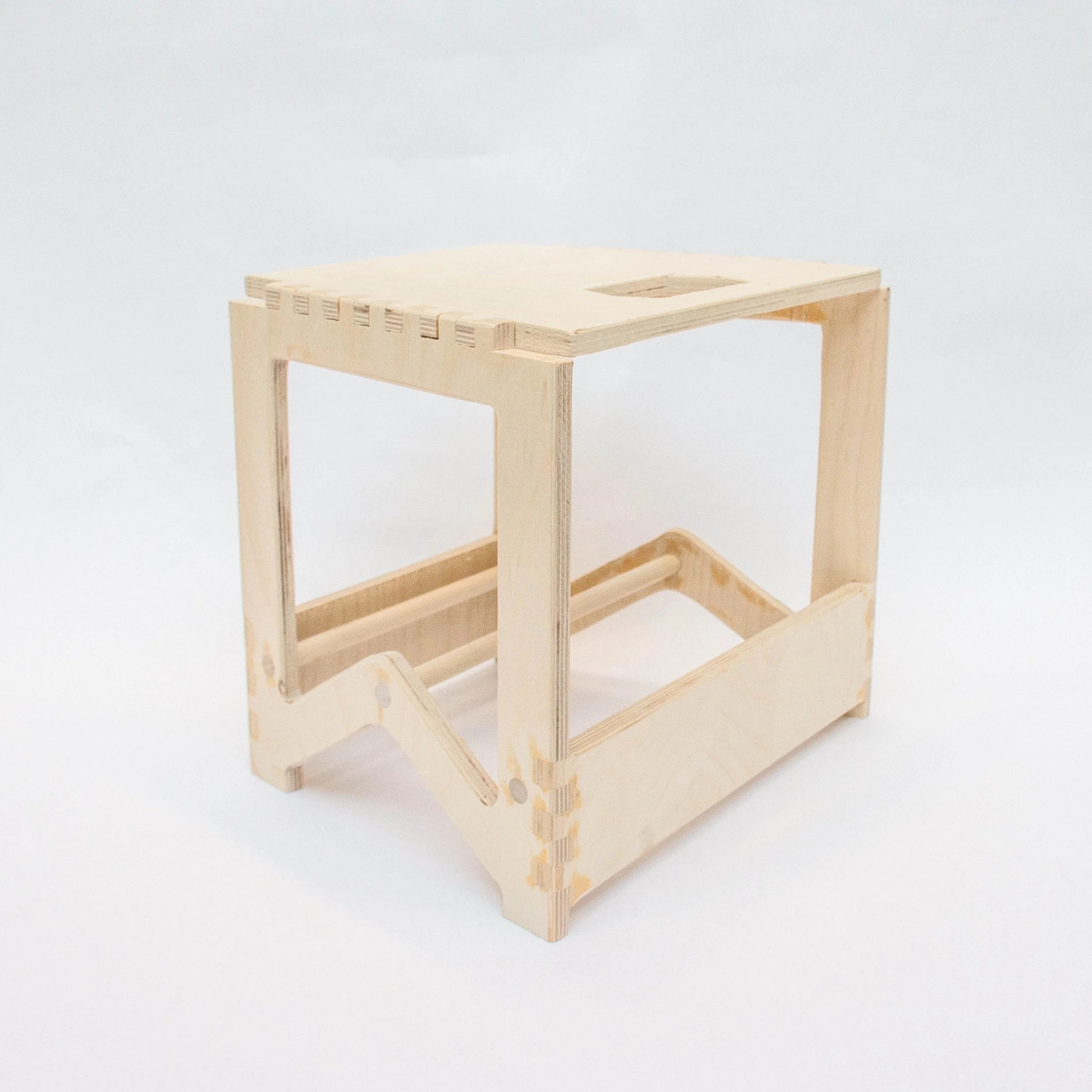 Small wooden table or stand with open sides and a flat top, made of light-colored wood, with visible joinery.